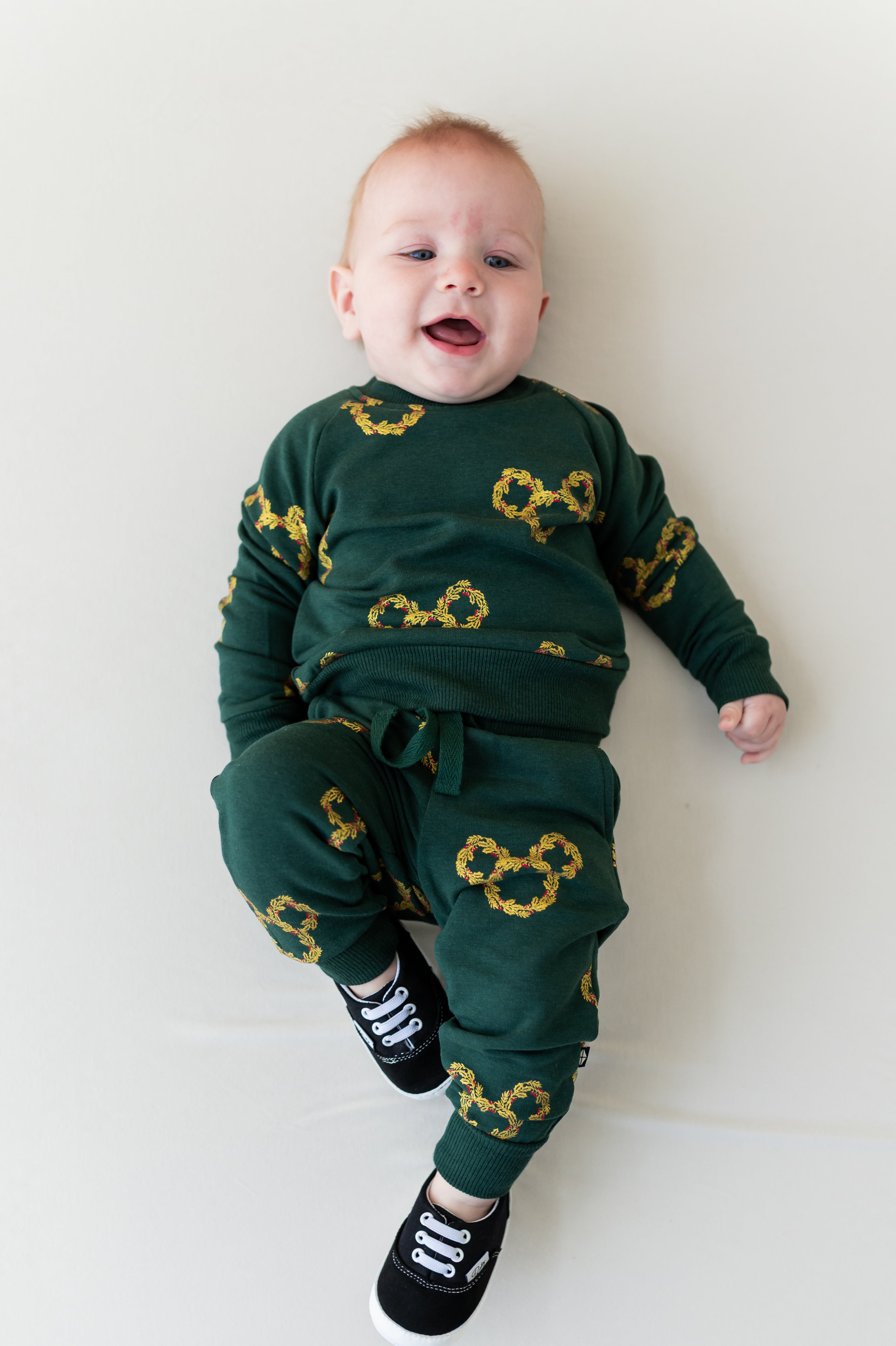 Baby wearing Long Sleeve Jogger Set in Mickey Christmas Wreath print lying on a white background