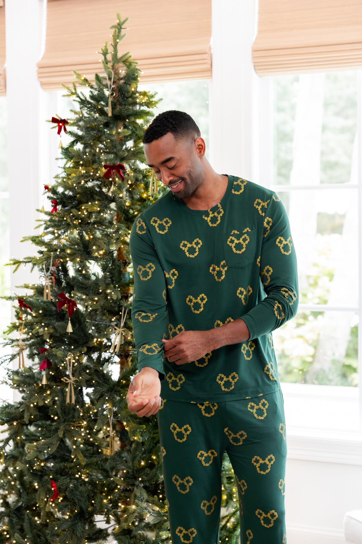 Modal wearing Men's Jogger Set in Mickey Christmas Wreath print standing beside a Christmas tree
