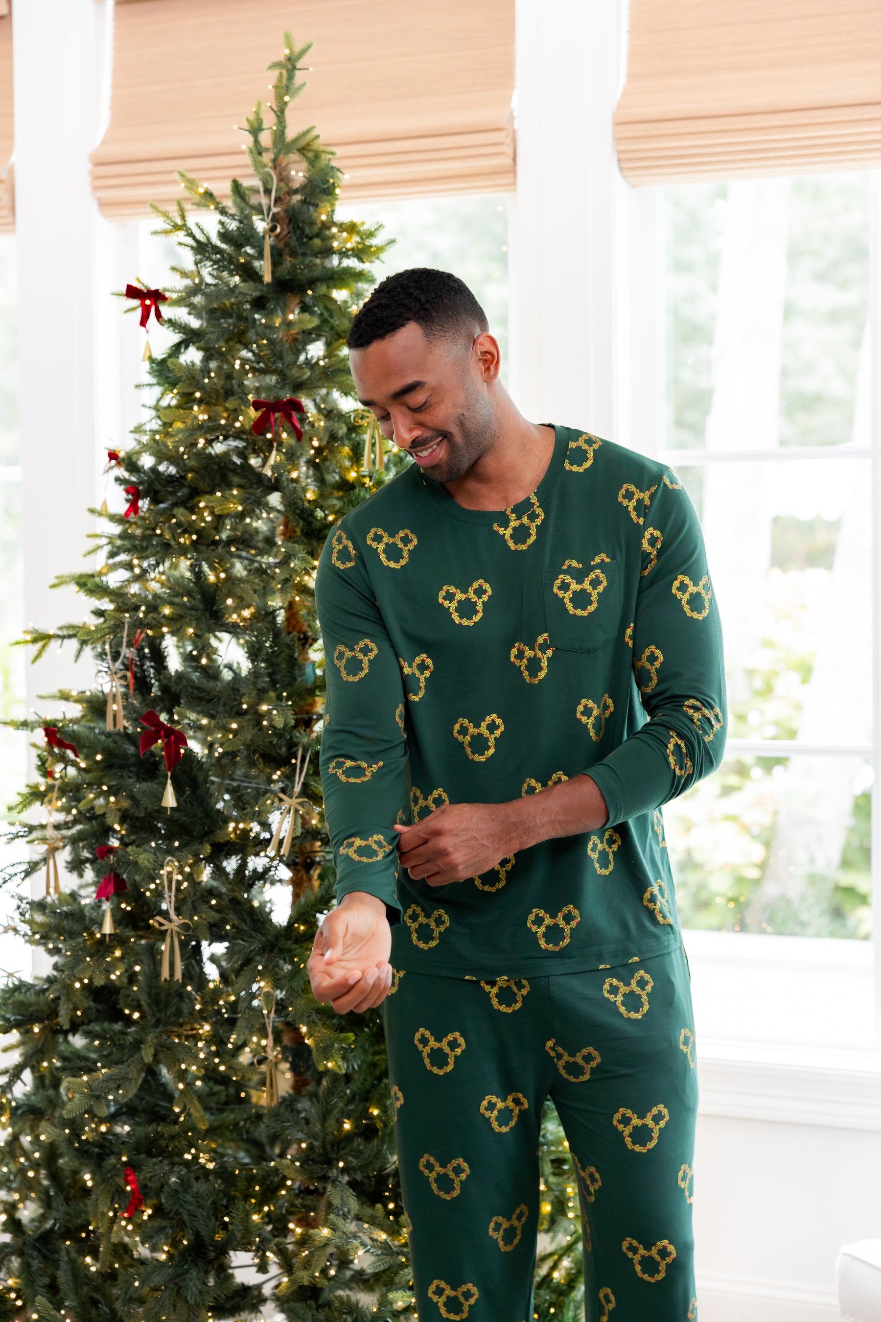 Modal wearing Men's Jogger Set in Mickey Christmas Wreath print standing beside a Christmas tree