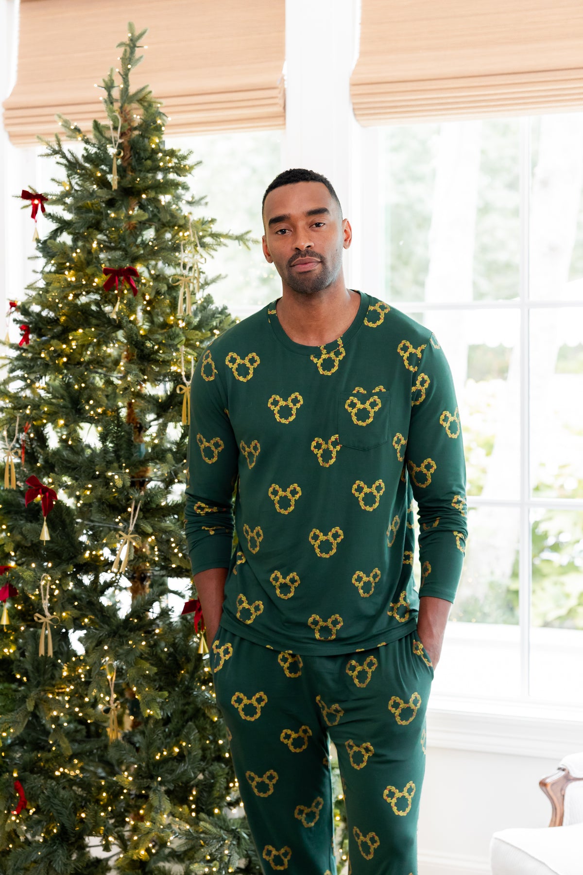 Modal wearing Men's Jogger Set in Mickey Christmas Wreath print standing beside a Christmas tree