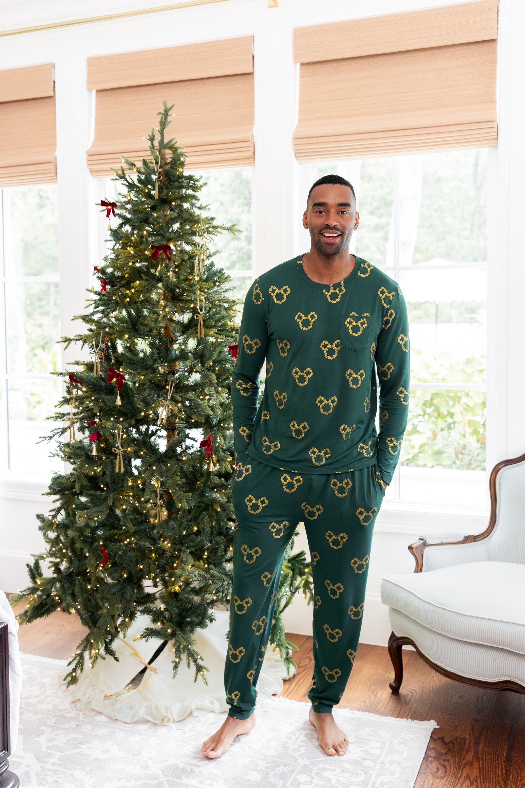 Modal wearing Men's Jogger Set in Mickey Christmas Wreath print standing beside a Christmas tree