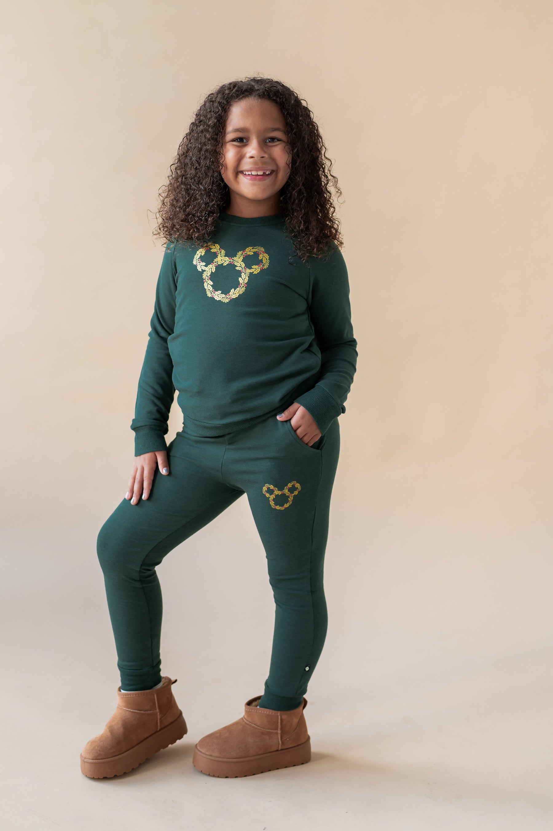 Girl wearing Long Sleeve Jogger Set in Mickey Christmas Wreath print in the center in Cypress color on a beige background