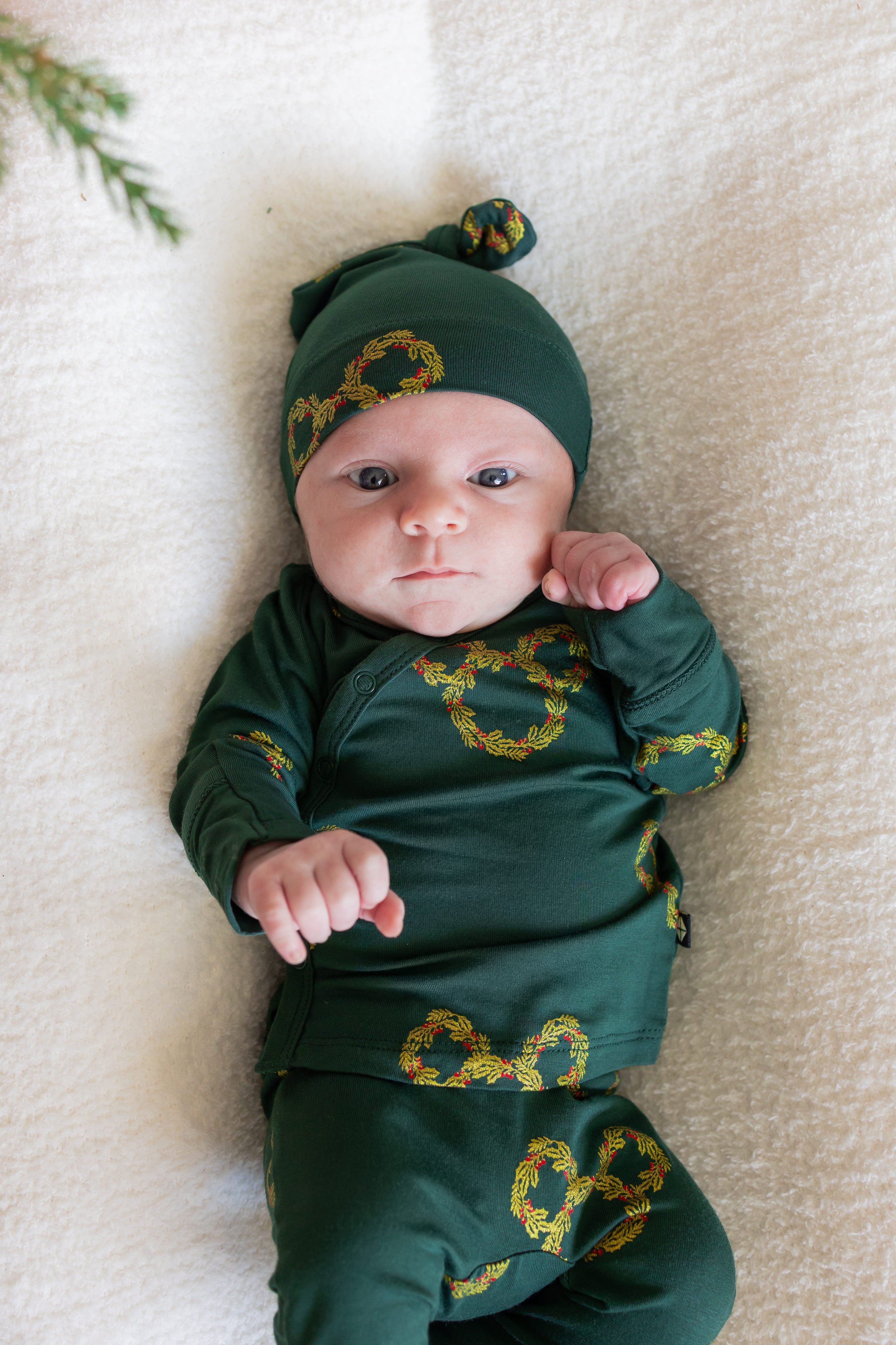 Baby wearing Take Me Home Set with Cap in Mickey Christmas Wreath print lying on white oval sheet