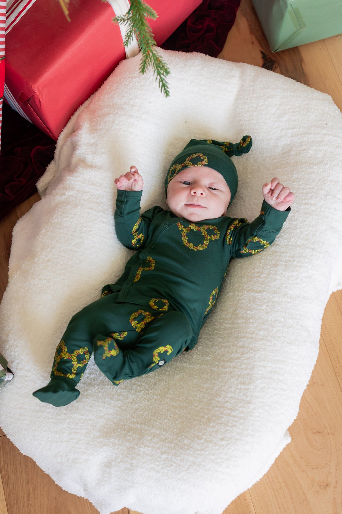Baby wearing Take Me Home Set with Cap in Mickey Christmas Wreath print lying on white oval sheet