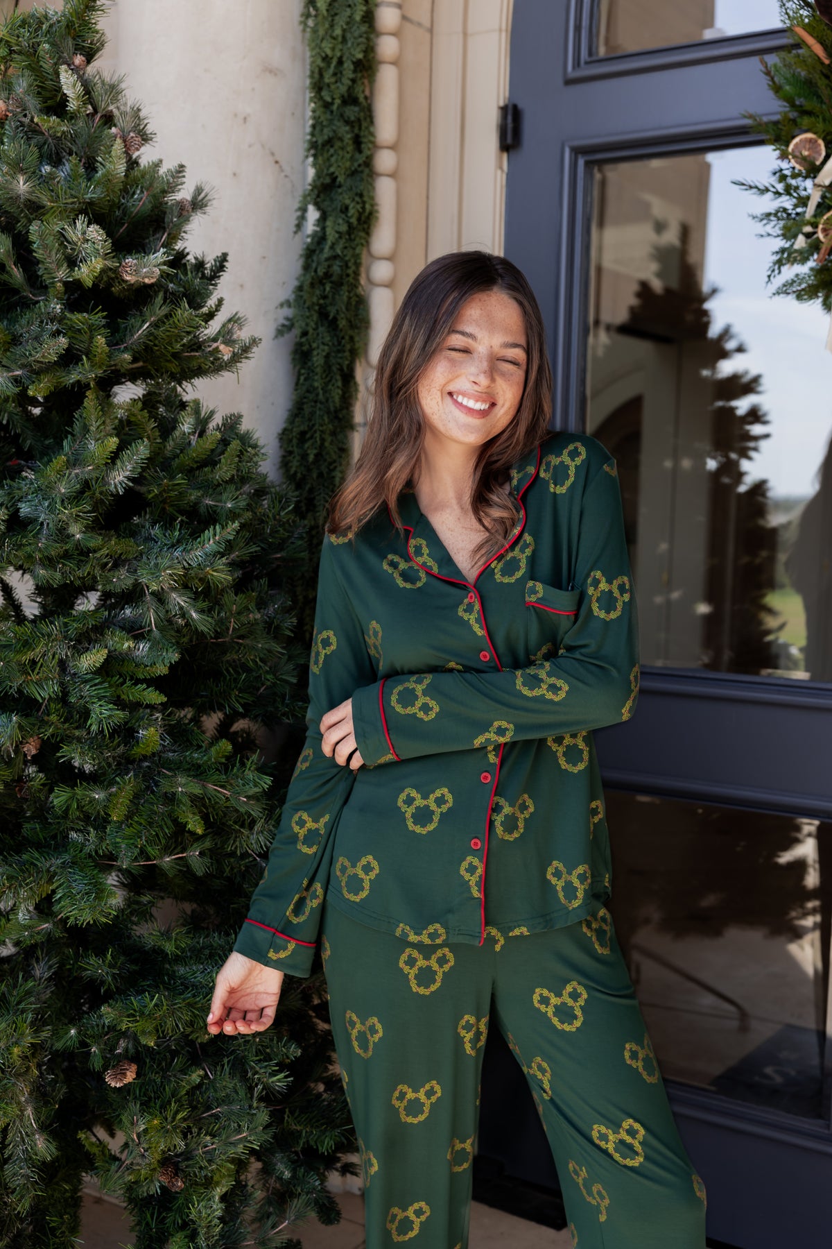 Women wearing Long-Sleeved Women's Pajama Set in Mickey Christmas Wreath print standing outdoors beside tree