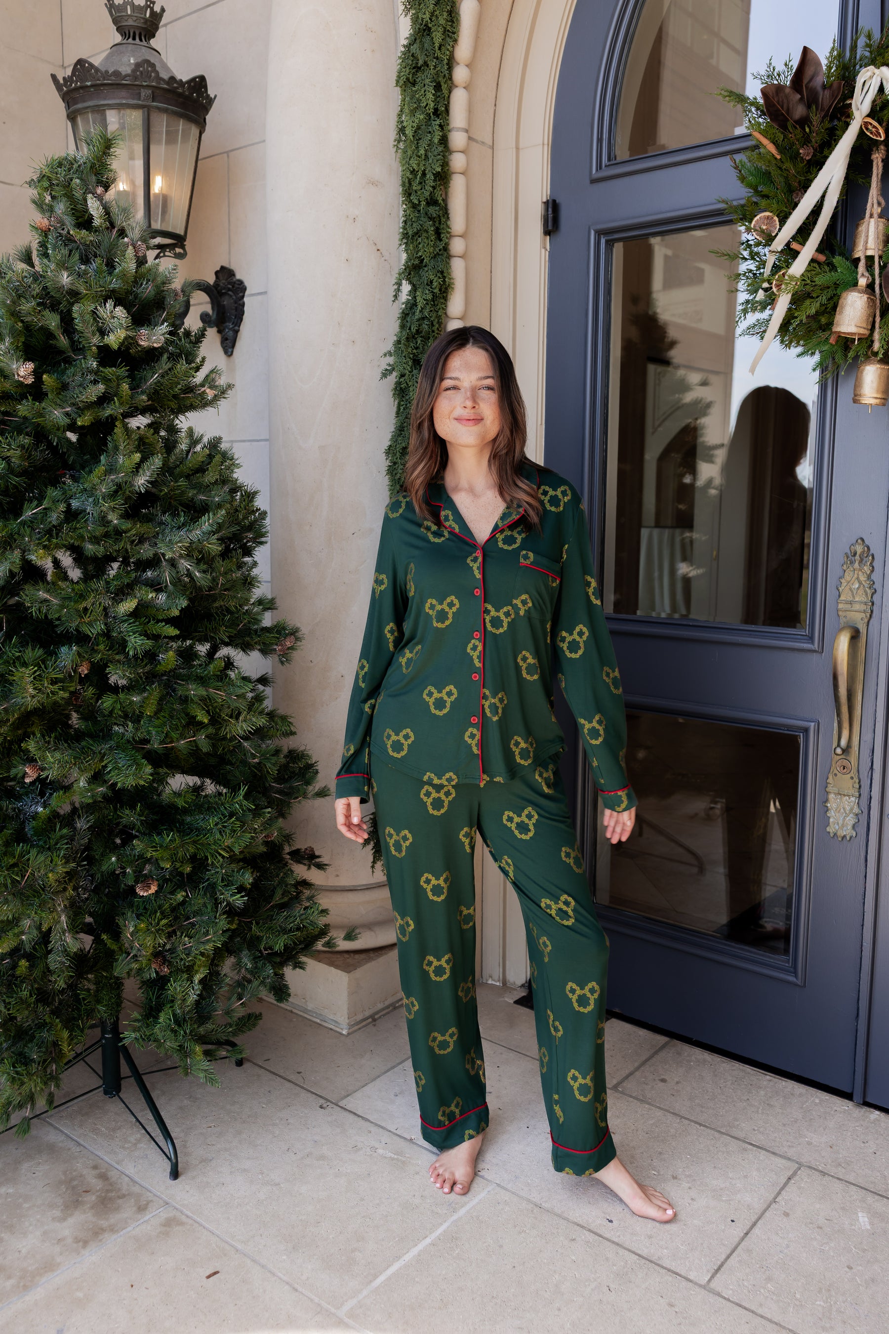 Women wearing Long-Sleeved Women's Pajama Set in Mickey Christmas Wreath print standing outdoors beside a tree