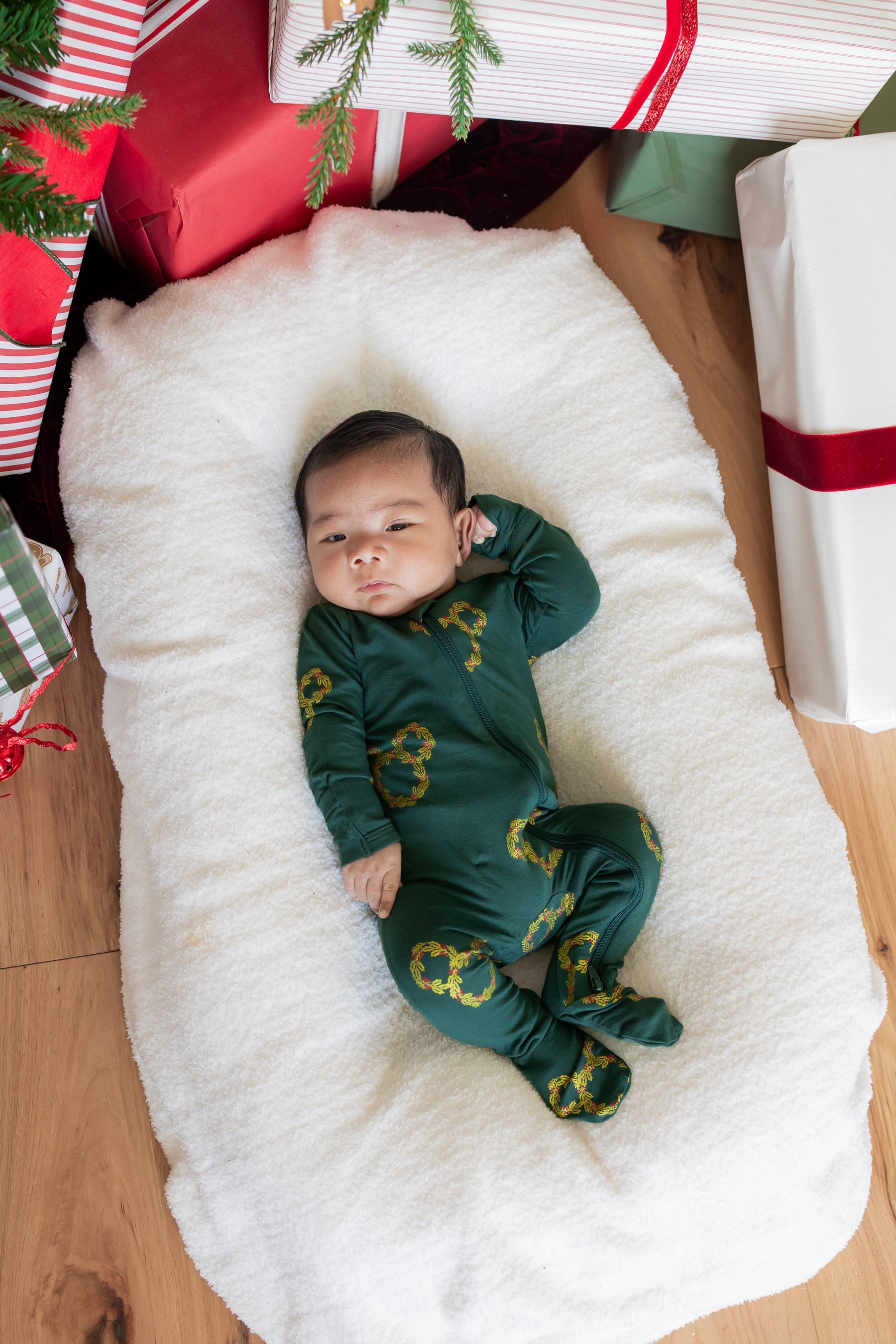Baby wearing Zippered Footie in Mickey Christmas Wreath print lying between presents