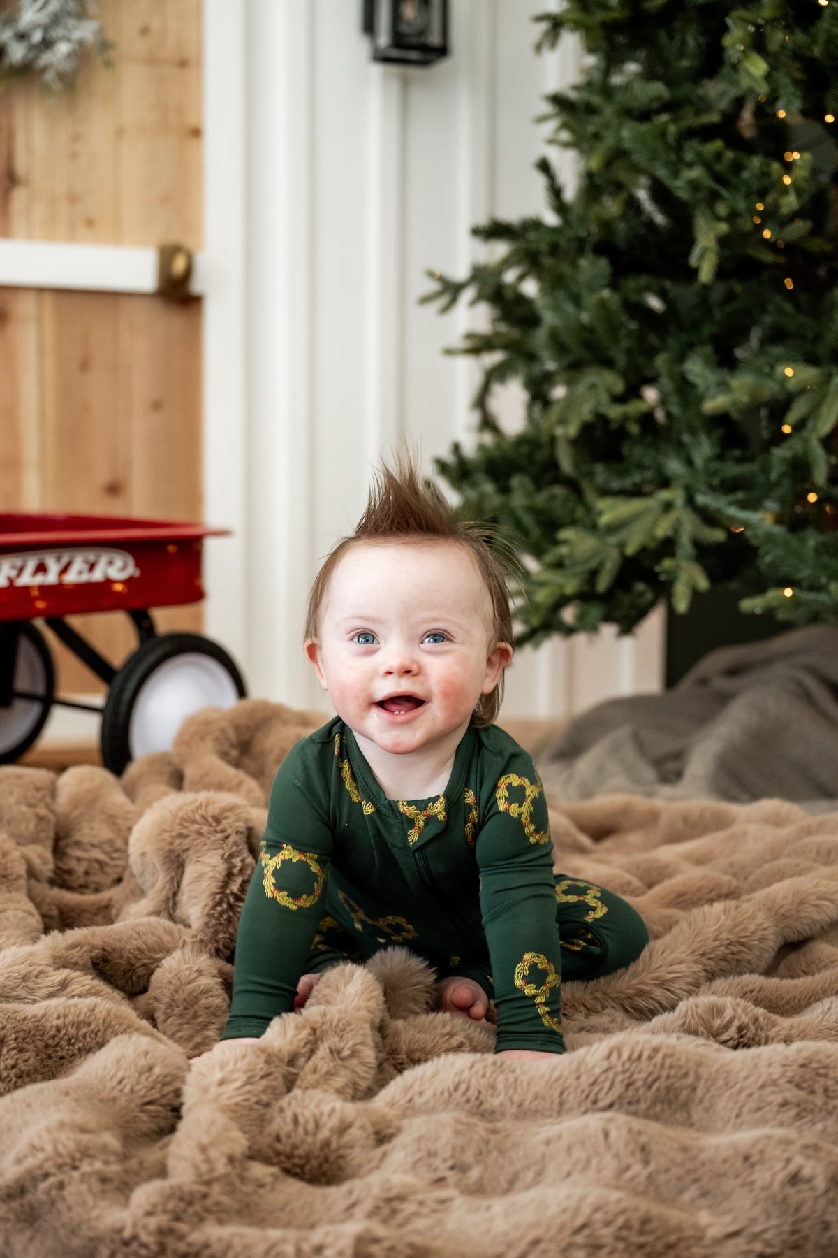 Baby wearing Zippered Romper in Mickey Christmas Wreath print sitting on a beige blanket
