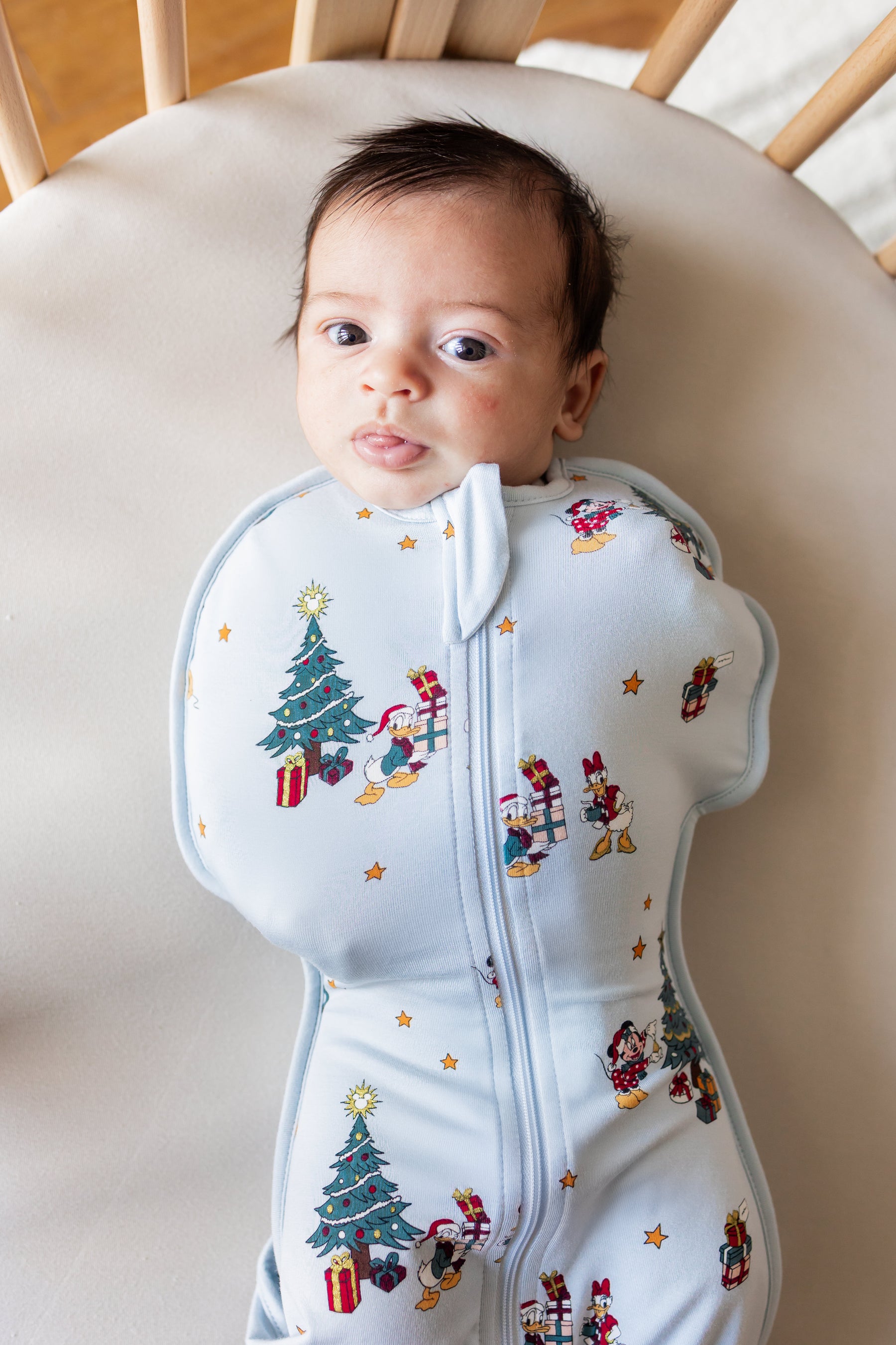 Baby in Swaddle Bag in Mickey & Friends Christmas 0.5 print lying on beige oval crib sheet