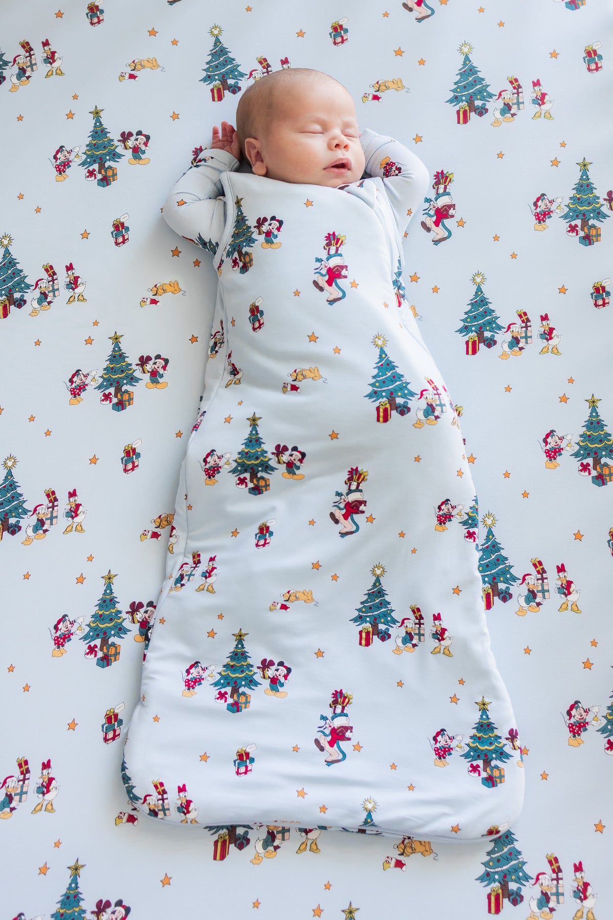 Baby sleeping in Sleep Bag in Mickey & Friends Christmas 1.0 print lying on similar print crib sheet