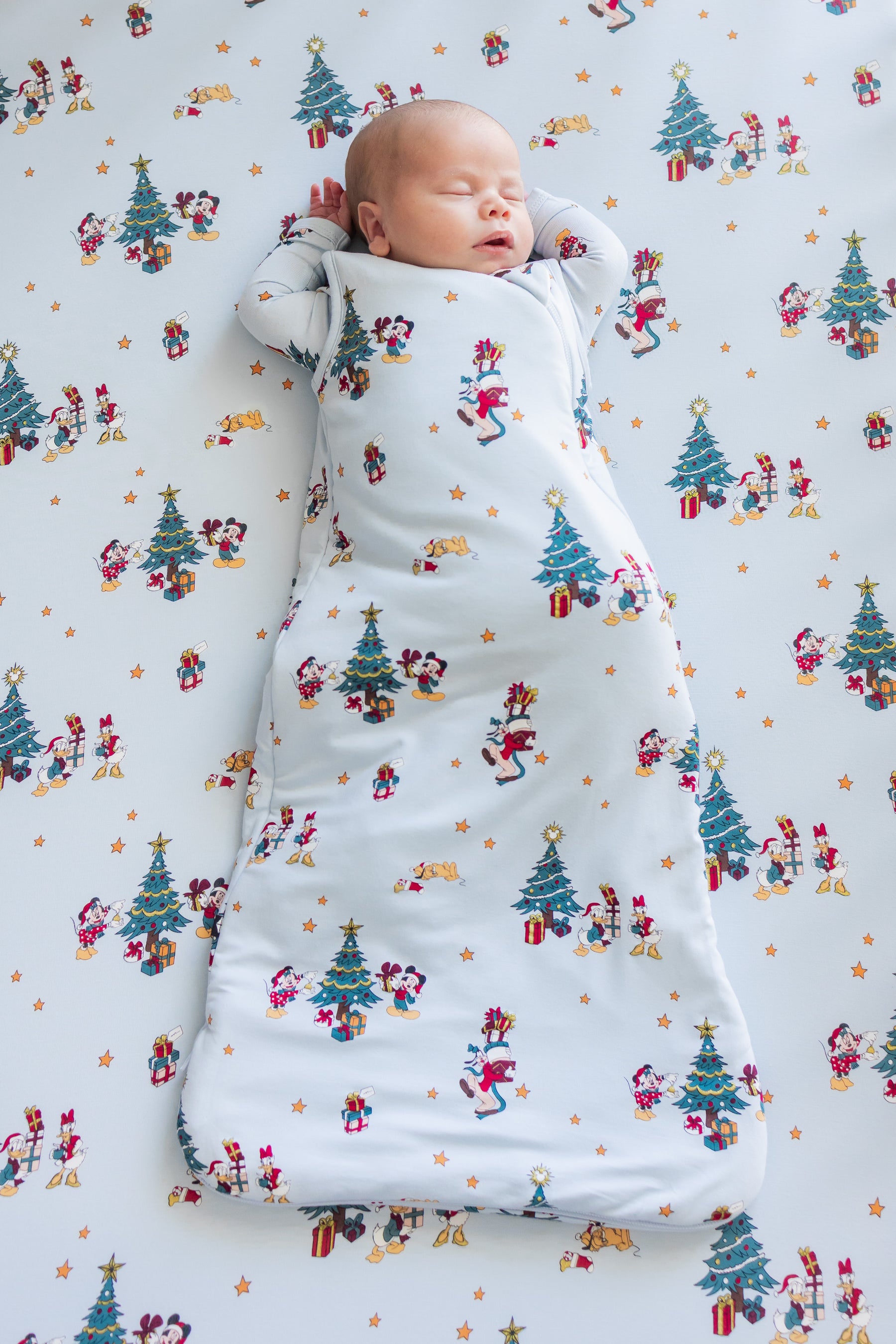 Baby sleeping in Sleep Bag in Mickey & Friends Christmas 1.0 print lying on similar print crib sheet