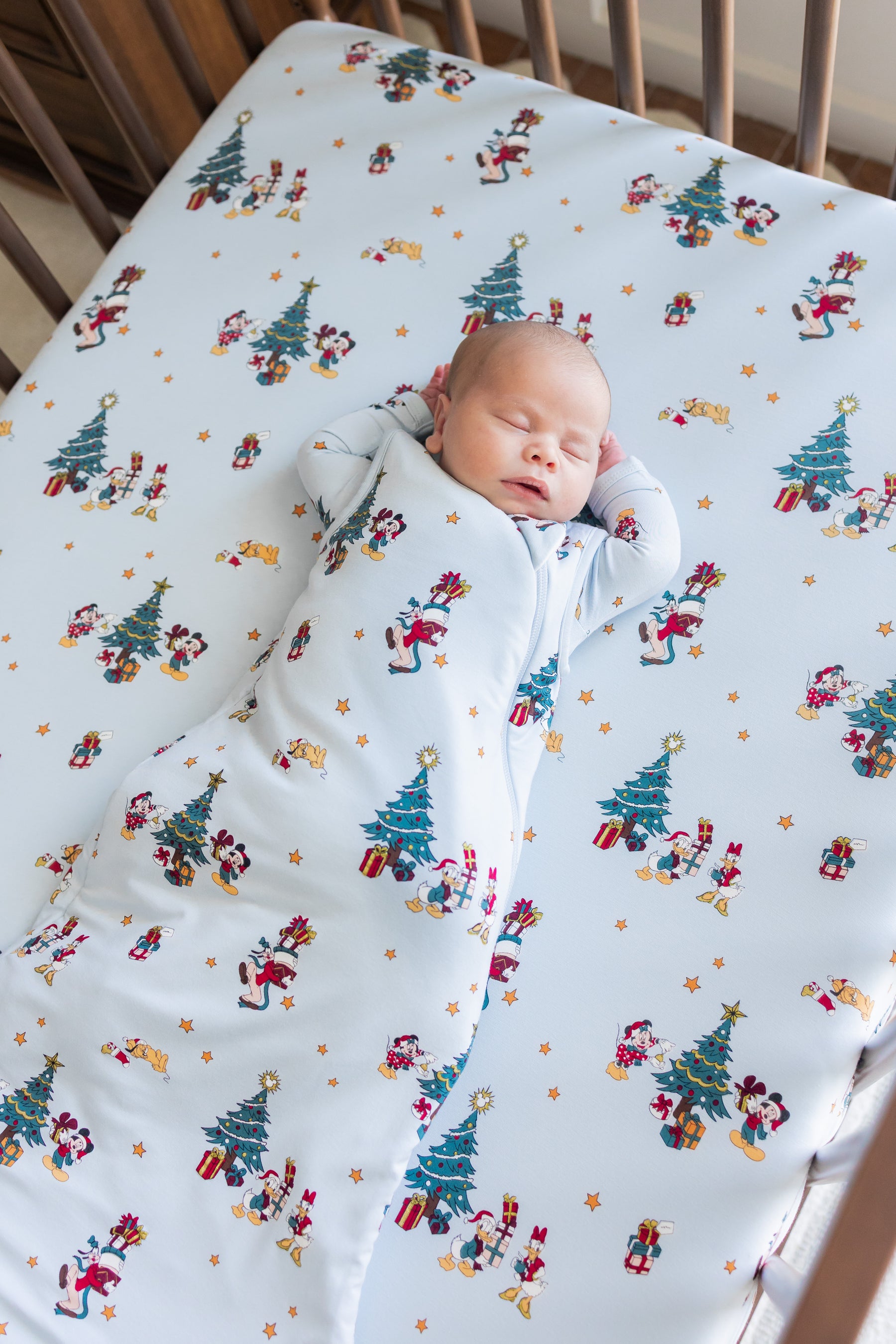 Baby sleeping in a crib wearing Sleep Bag in Mickey & Friends Christmas 1.0 print lying on similar print crib sheet