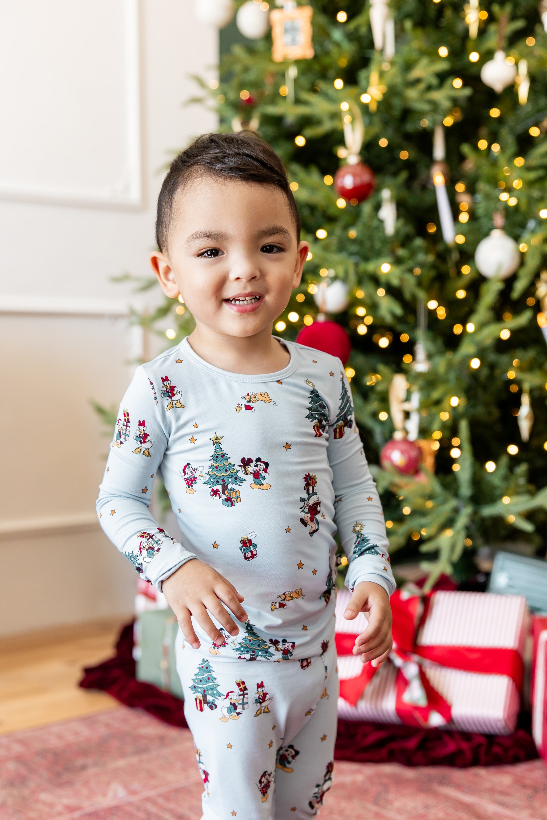 Boy standing in front of Christmas tree and presents wearing Long Sleeve Pajamas in Mickey & Friends Christmas print