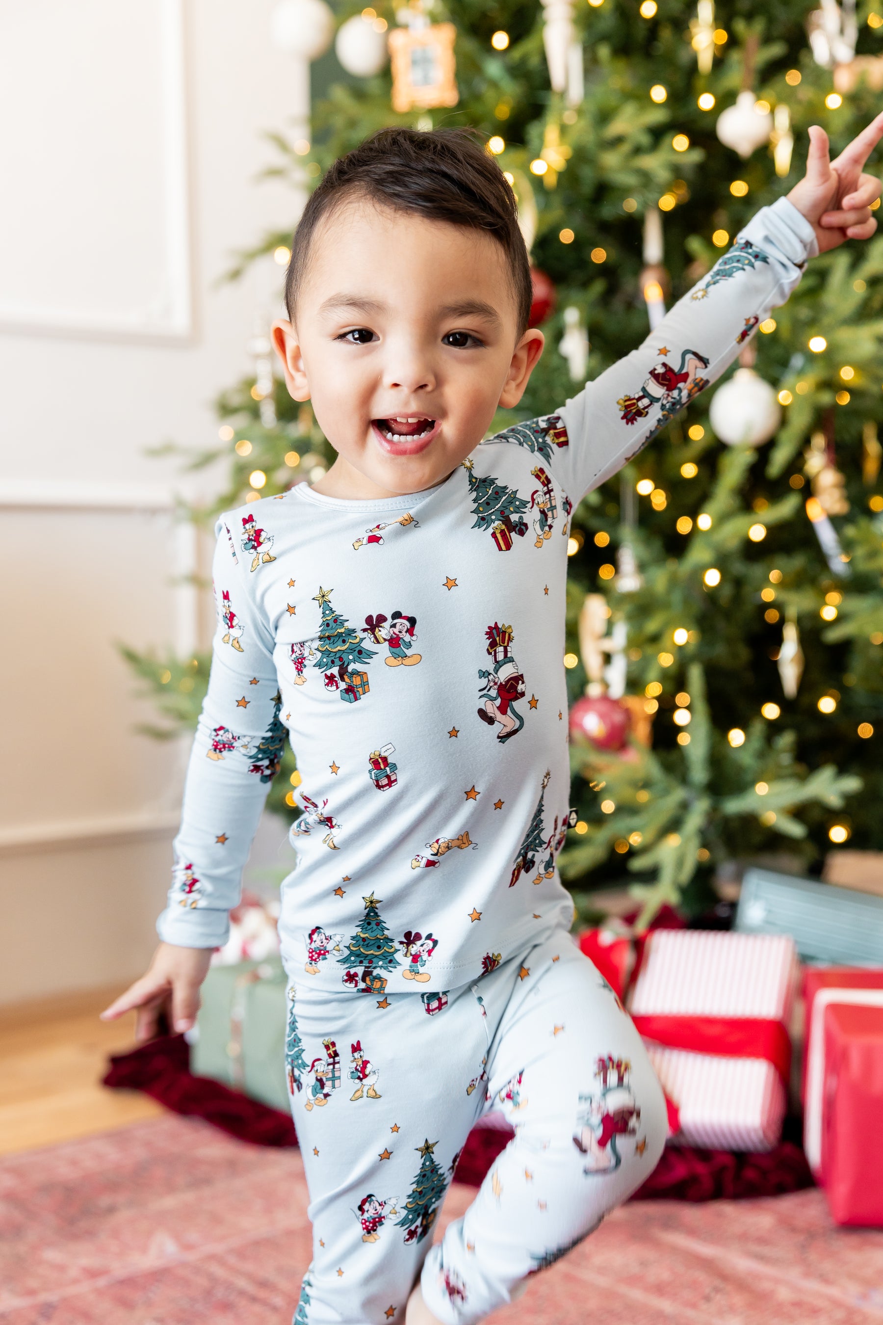 Boy posing in front of Christmas tree and presents wearing Long Sleeve Pajamas in Mickey & Friends Christmas print