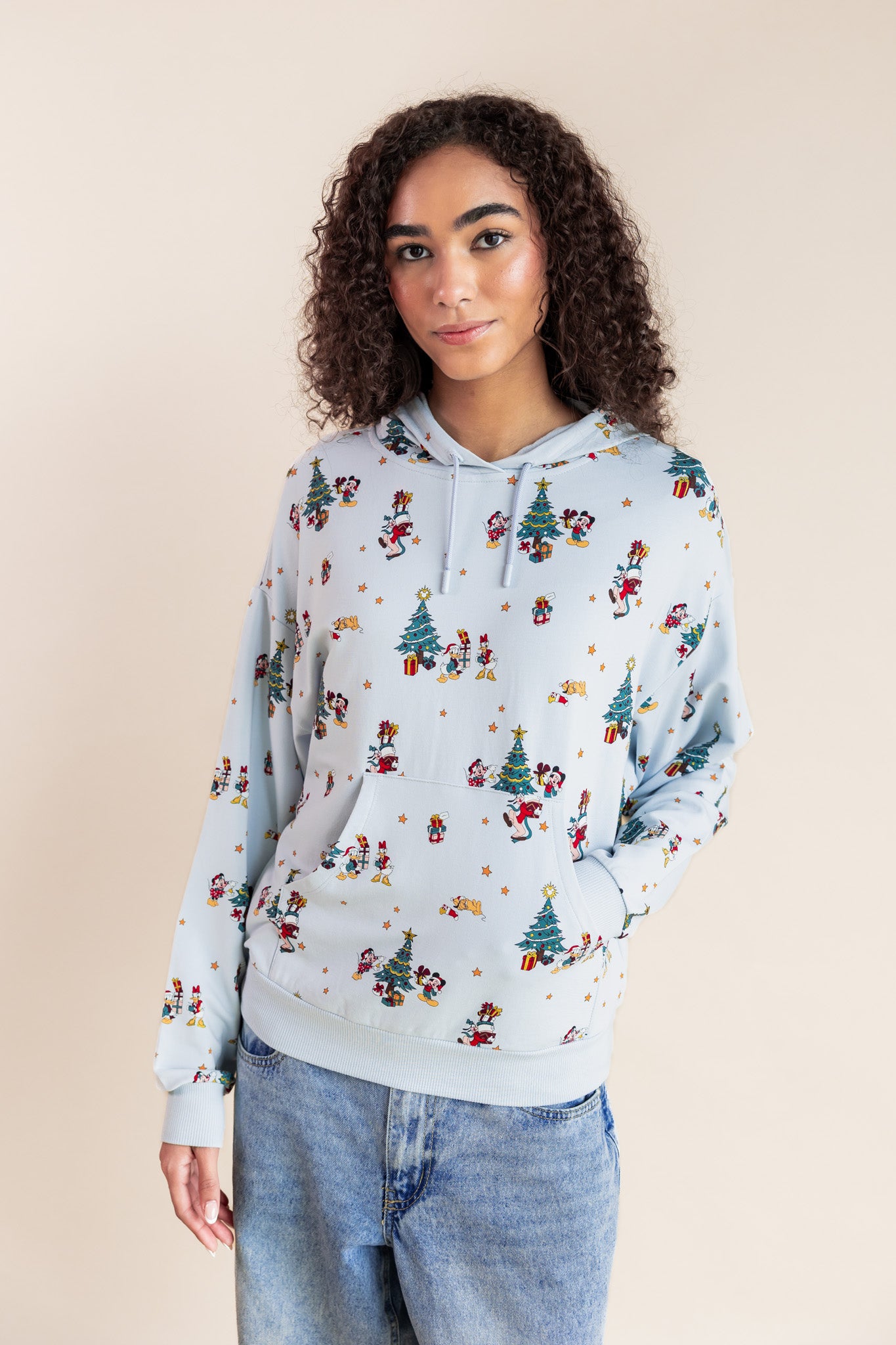 Woman wearing Women's Hoodie in Mickey & Friends Christmas print over blue jeans on a beige background