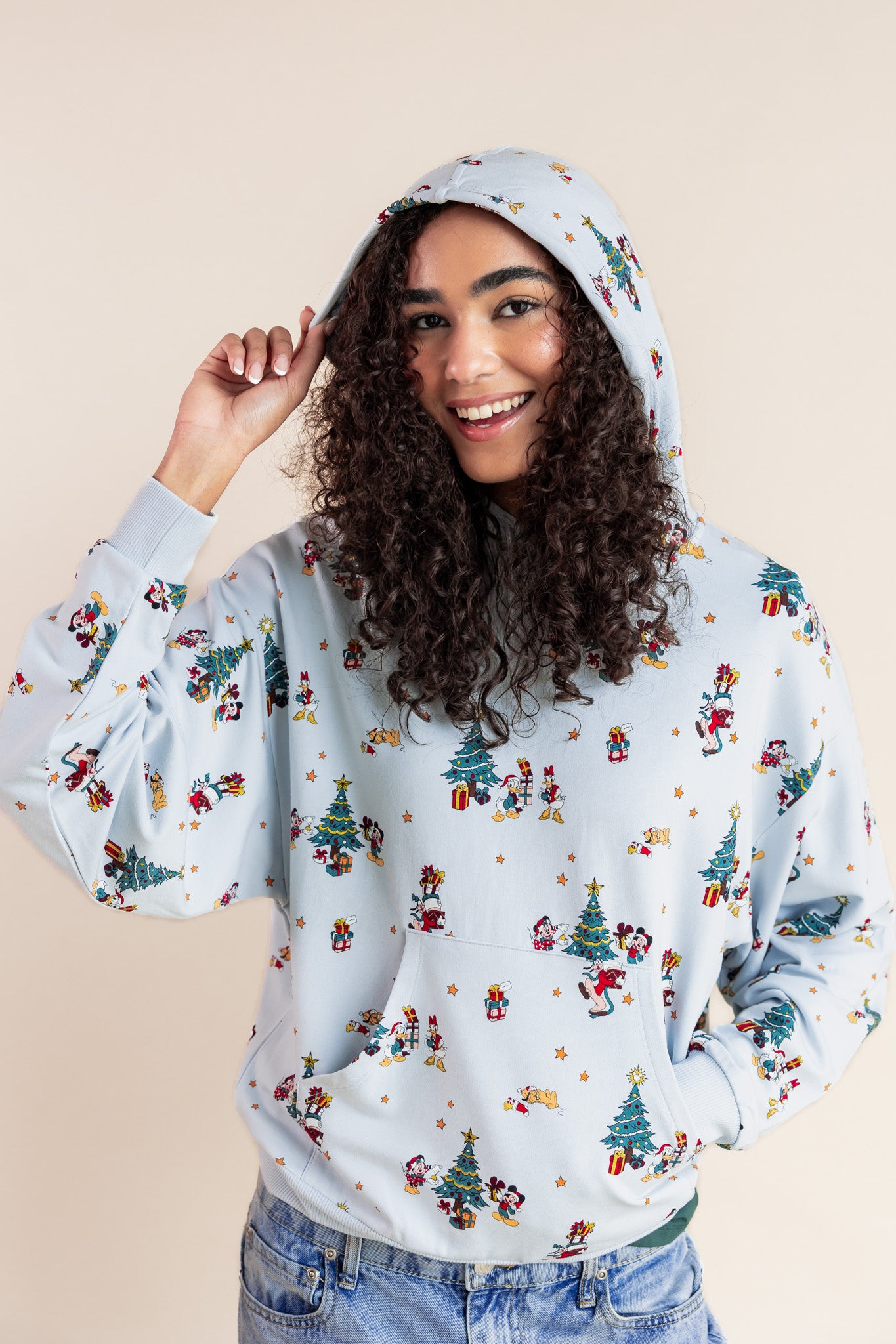 Woman wearing Women's Hoodie in Mickey & Friends Christmas print over blue jeans on a beige background