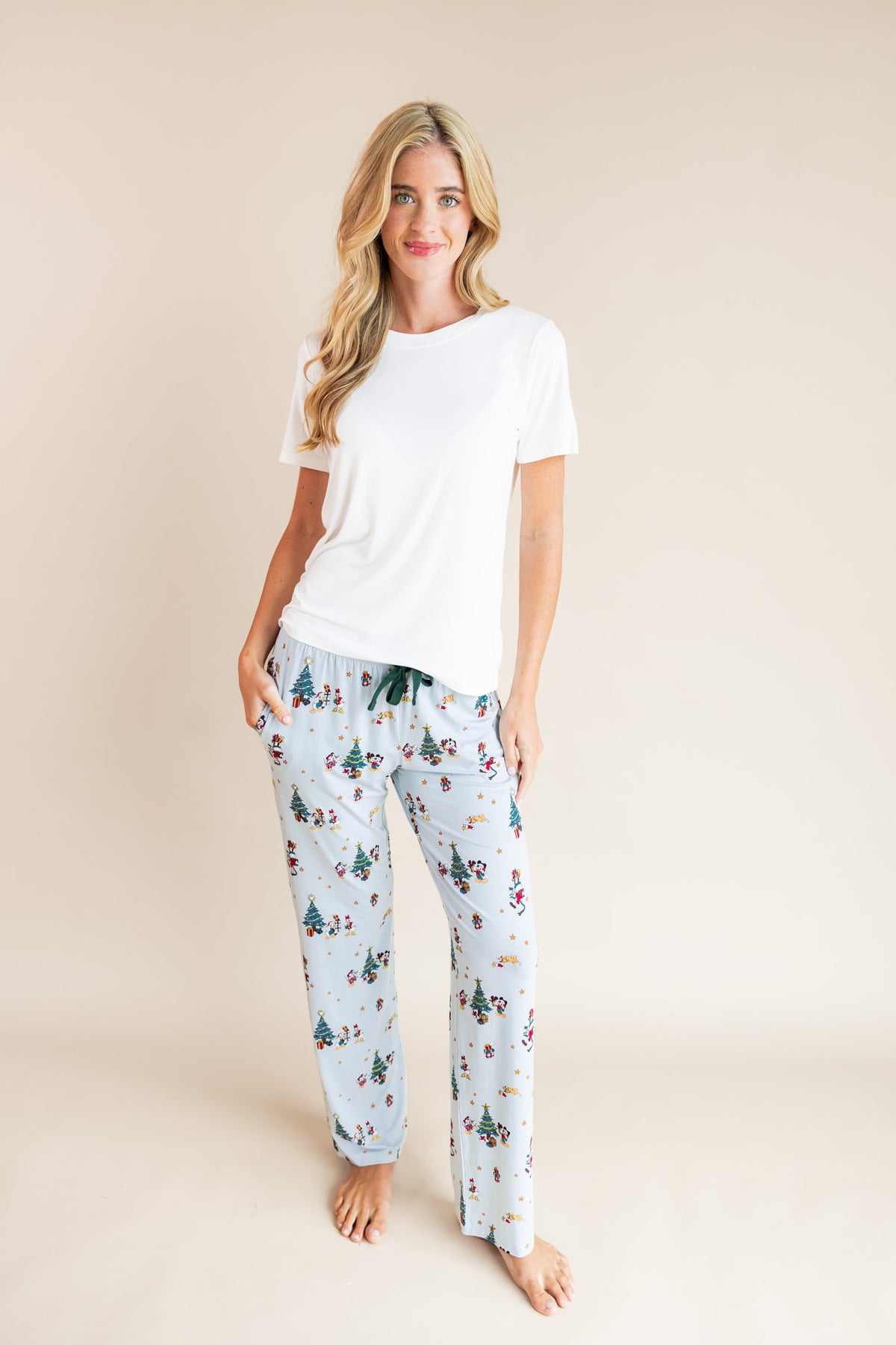 Woman wearing Women's Lounge Pants in Mickey & Friends Christmas print under white T-shirt on a beige background