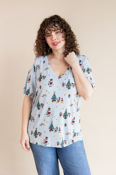 Woman wearing Women's Oversized V-Neck Tee in Mickey & Friends Christmas print over blue jeans on a beige background
