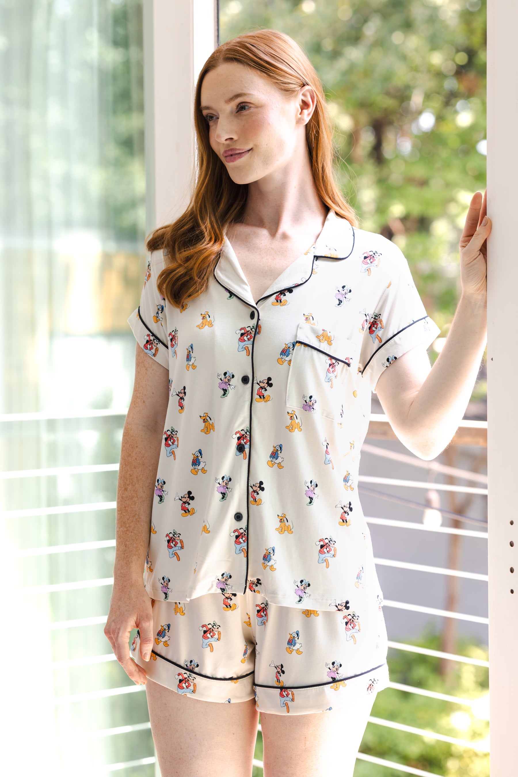 Model posing Women's Short Sleeve Pajama Set in Mickey Mouse & Friends print standing in front of glass door