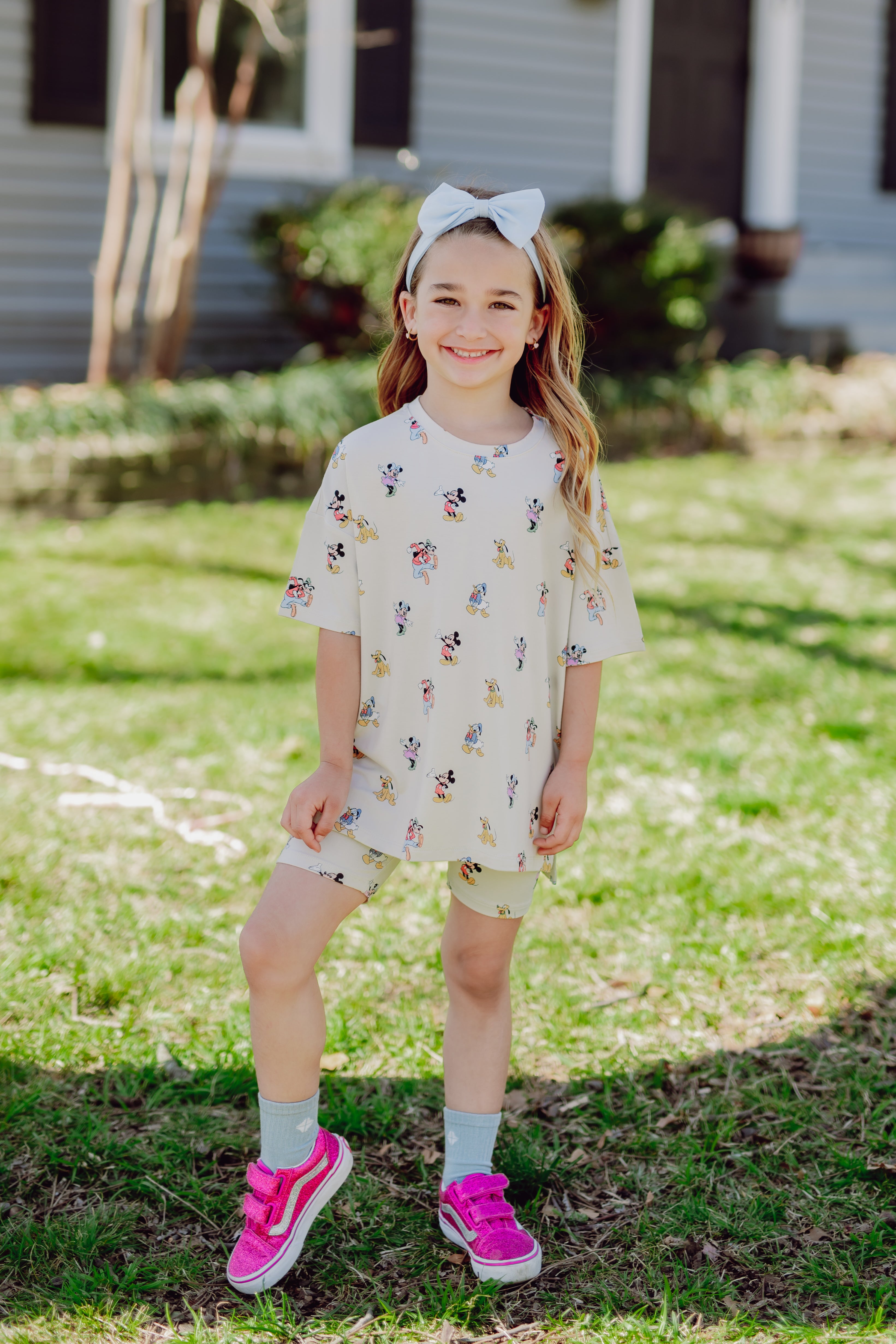 Young girl in a mickey and friends matching biker set and hot pink sneakers in front of a house
