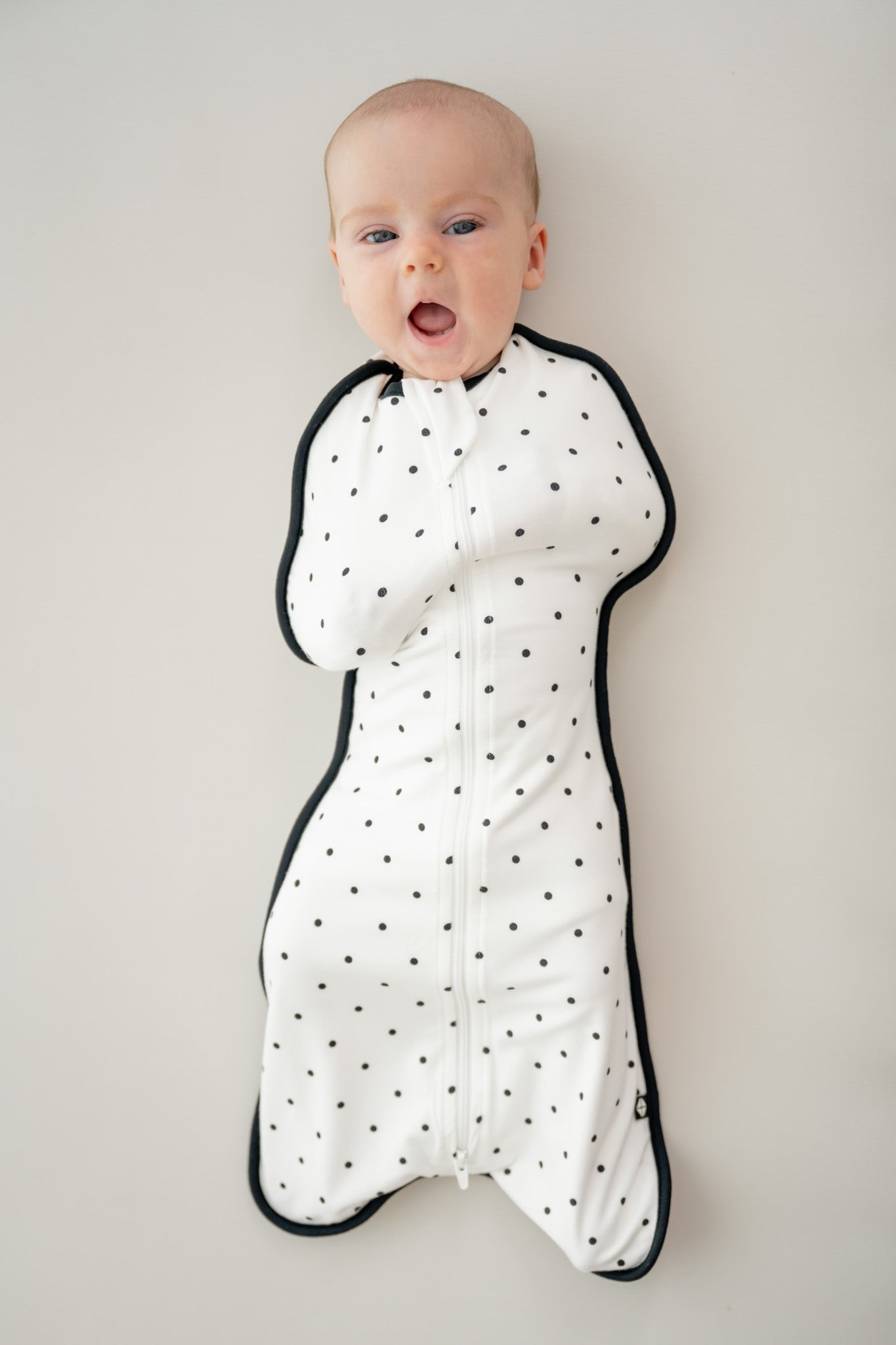 Baby wearing Swaddle bag in Midnight Polka Dot print on a beige background