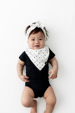 Baby wearing Midnight Polka Dot print Bib and Bow headband over a black bodysuit on a white background