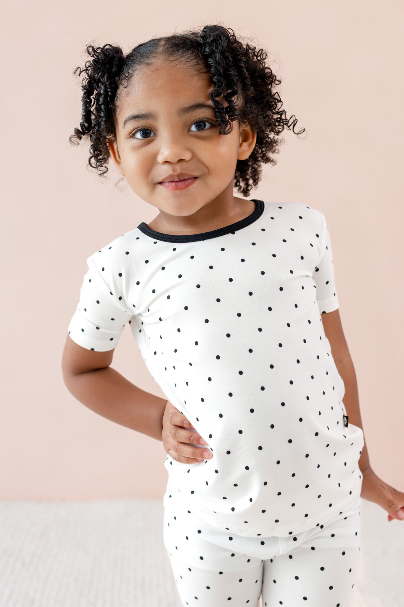 Child posing in Toddler Short Sleeve pajama set in Midnight Polka Dot print on a beige background