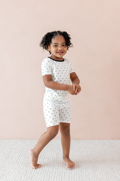 Child wearing Toddler Short Sleeve pajama set in Midnight Polka Dot print with black trim on the neck on a beige background