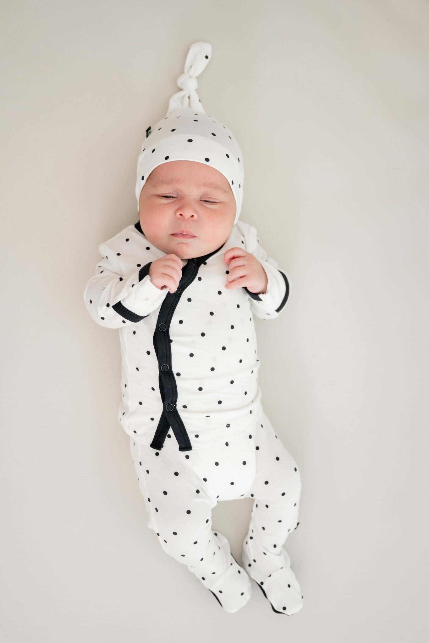 Baby sleeping in Midnight Polka Dot print take me home set with cap on a beige background
