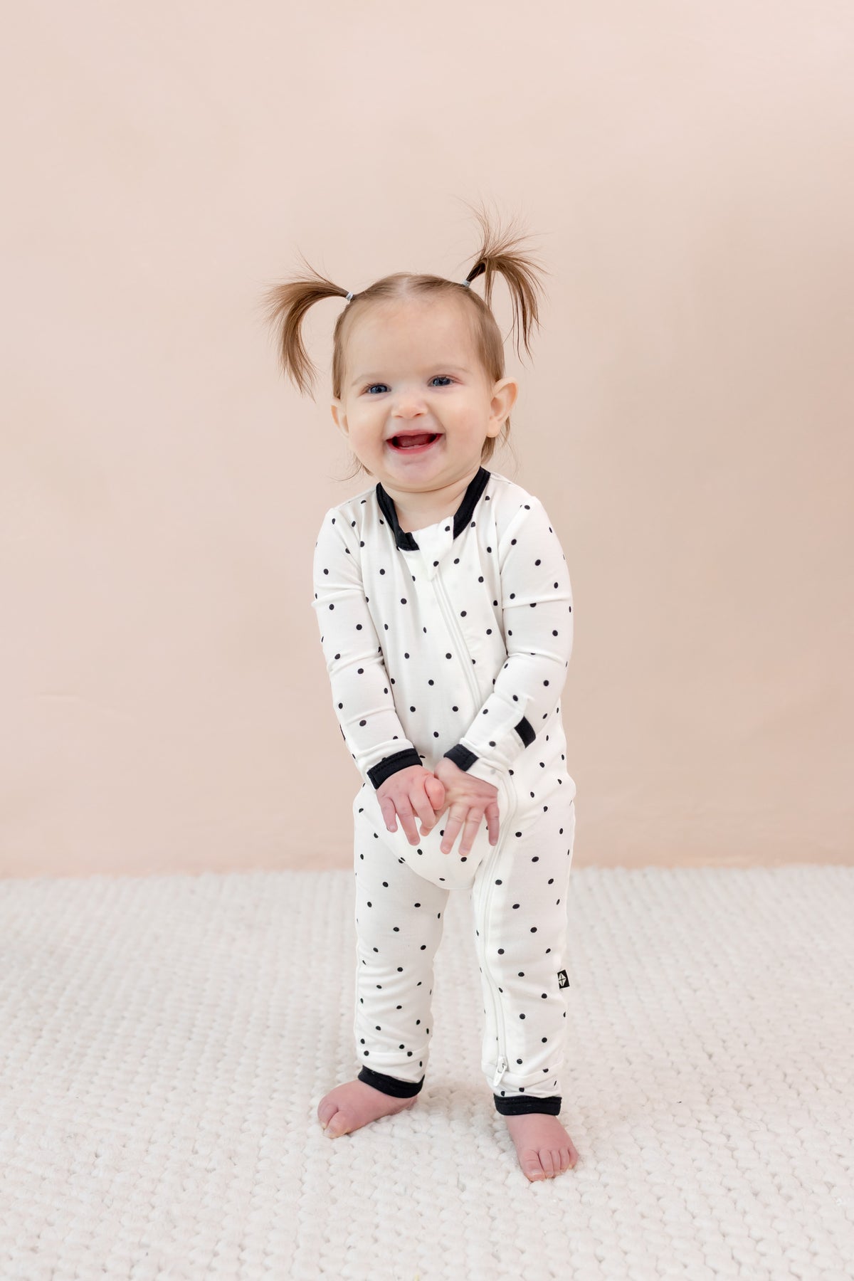 Child wearing zippered romper in midnight polka dot print on beige background