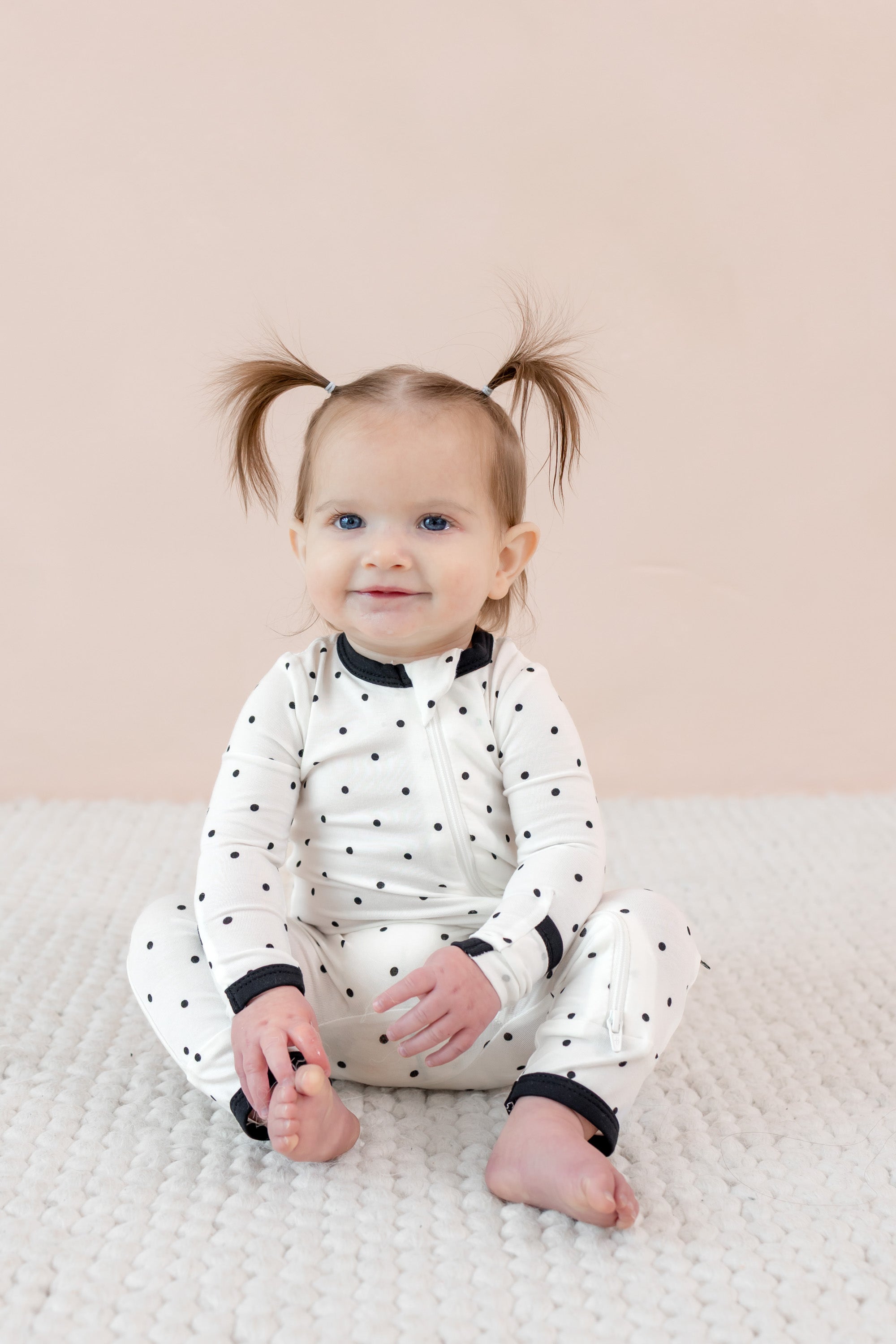 Child sitting in zippered romper with midnight polka dot print on beige background.