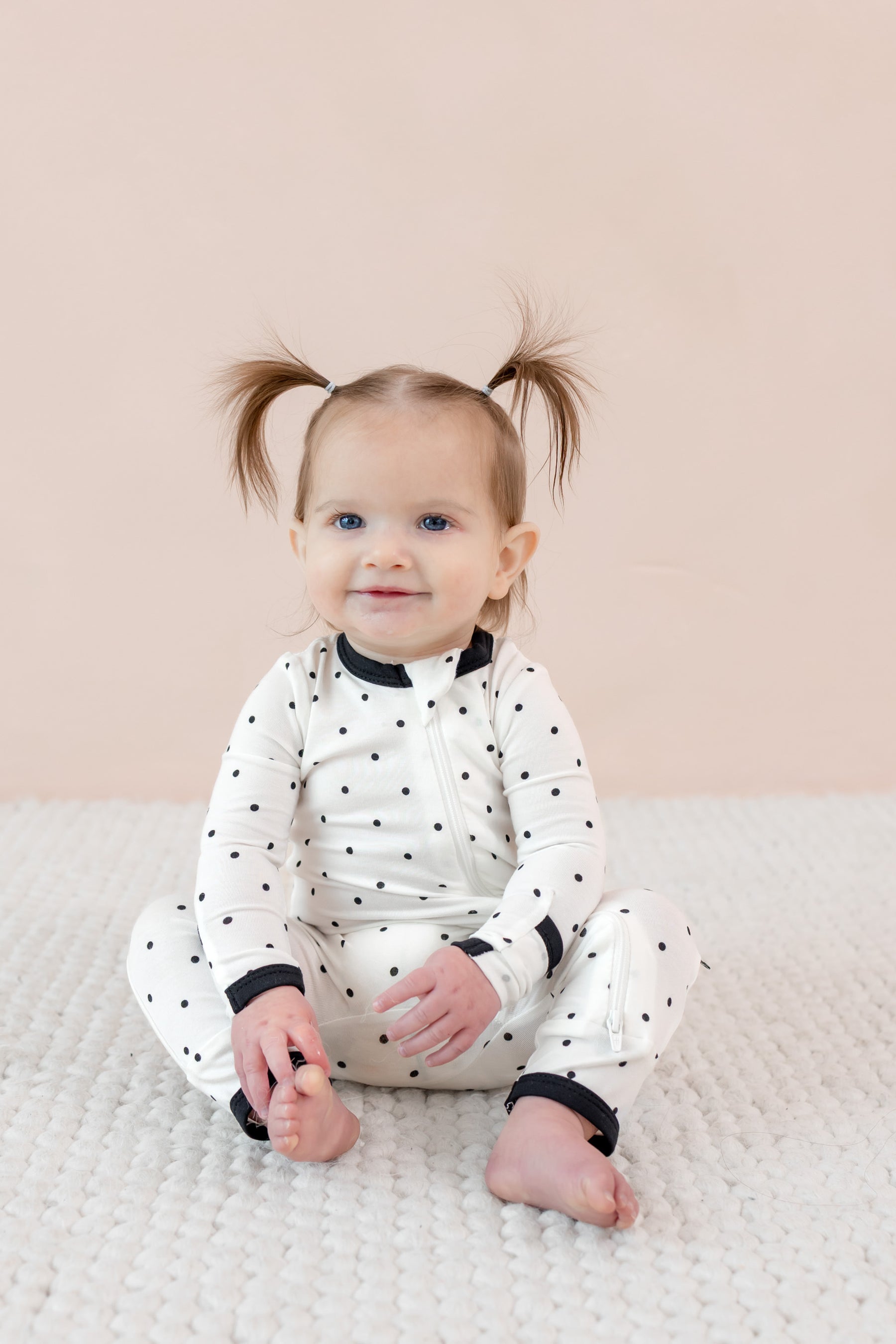 Child sitting in zippered romper with midnight polka dot print on beige background.
