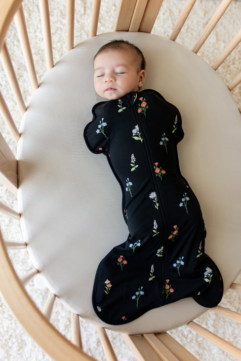 Baby sleeping in a crib wearing black Swaddle Bag with Wildflower print