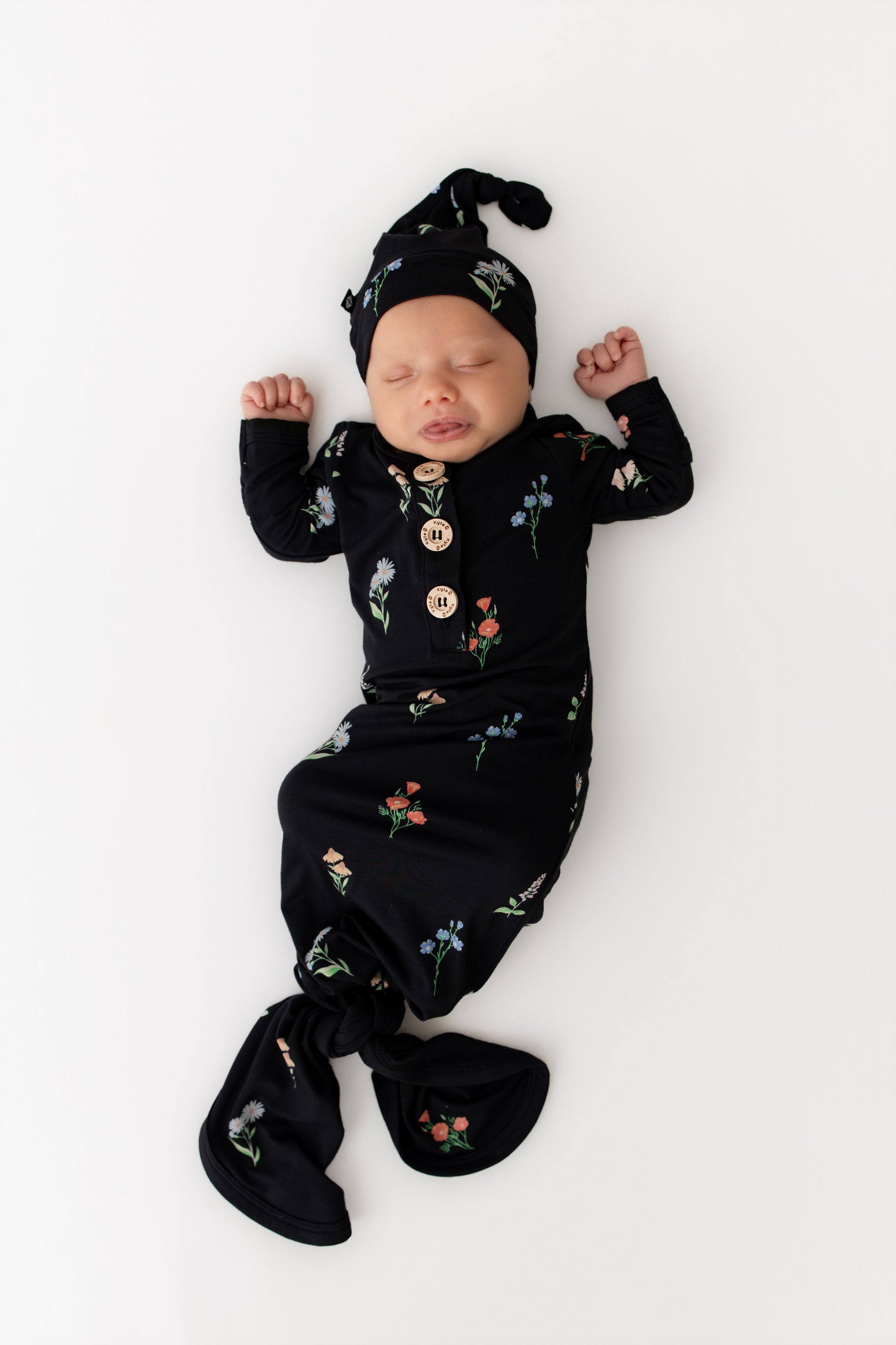 Baby sleeping in Knotted Gown with Hat Set in Midnight Wildflower print on a white background
