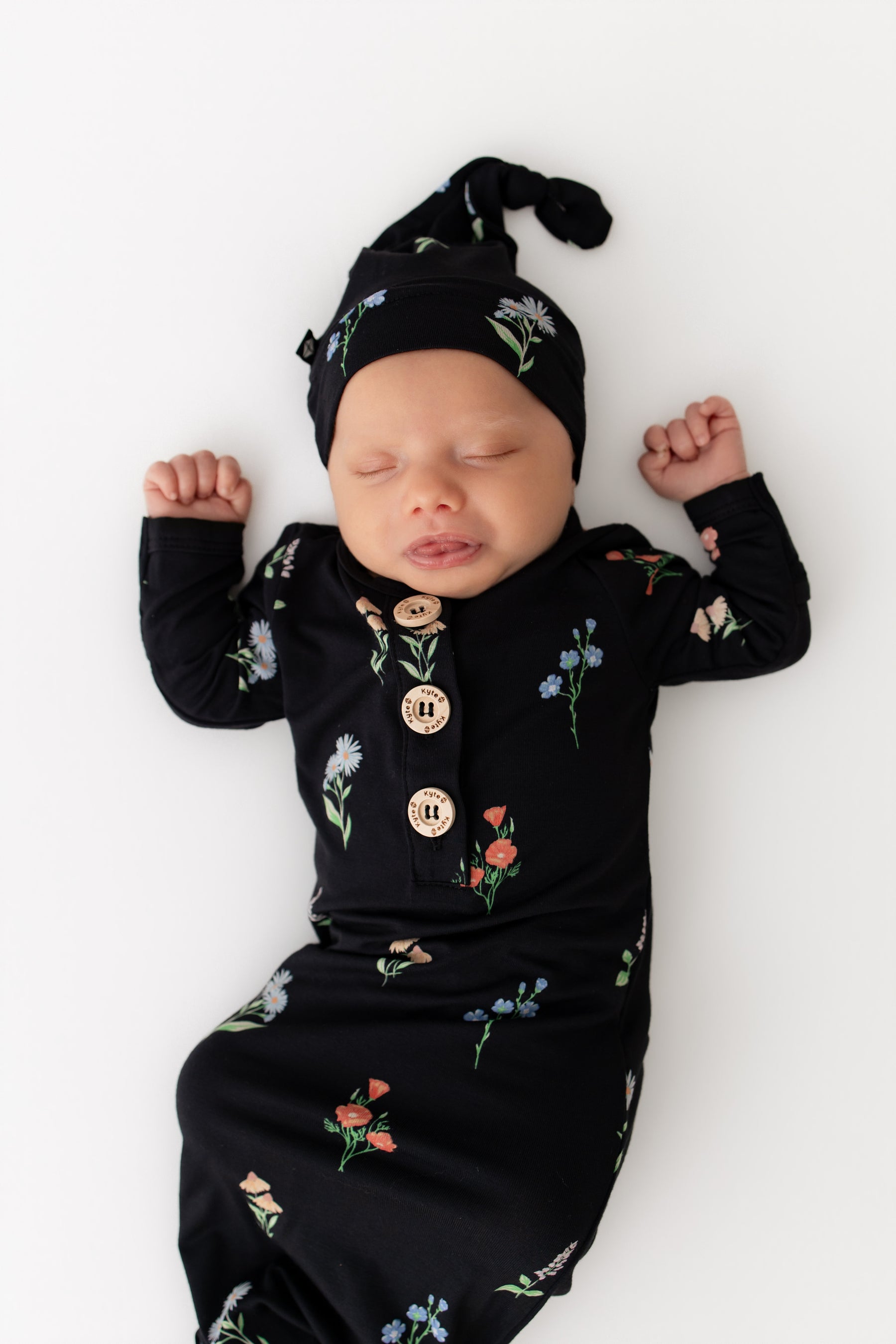Baby in Knotted Gown with Hat Set in Midnight Wildflower print on a white background