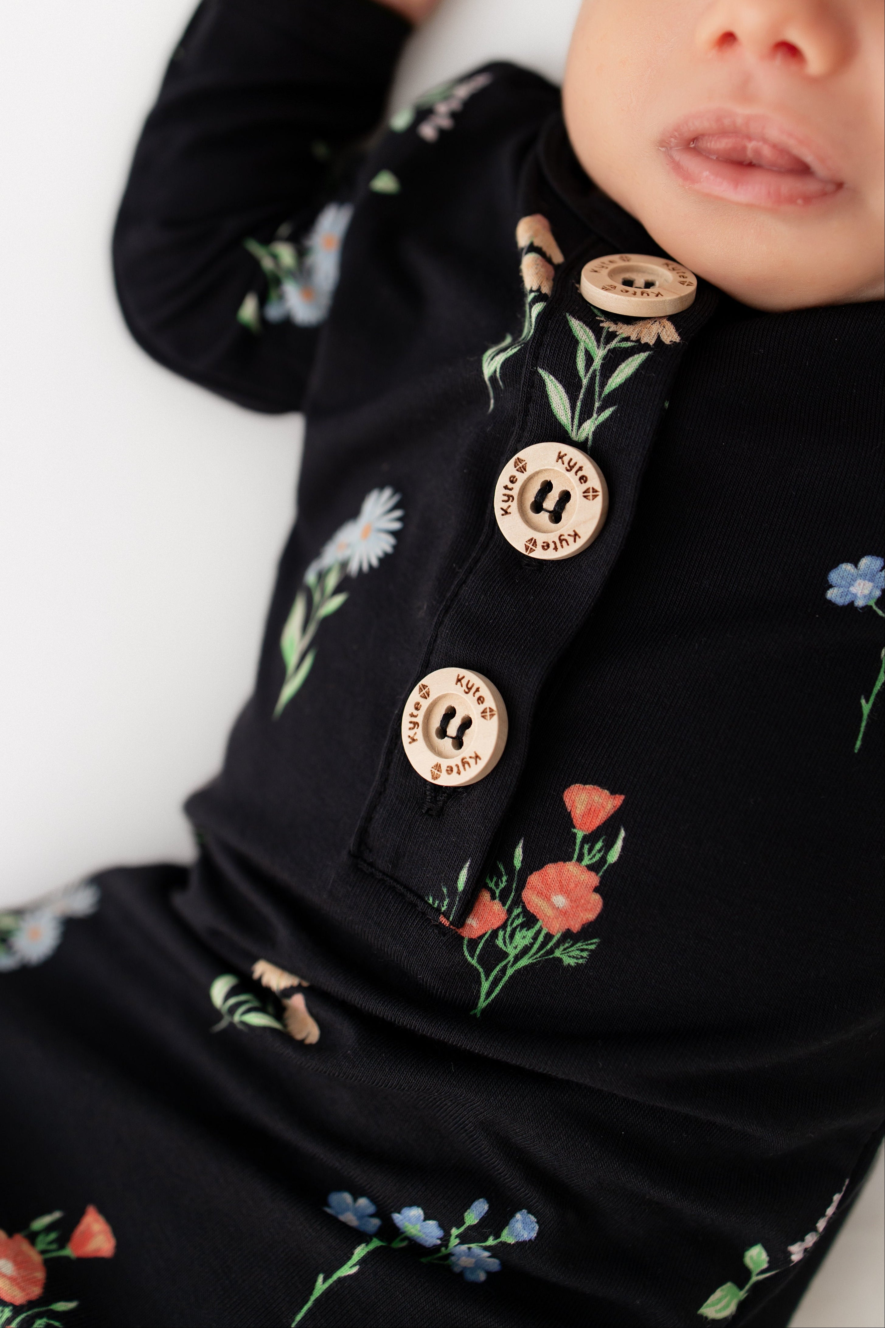 Baby sleeping in Knotted Gown with Hat Set in Midnight Wildflower print on a white background