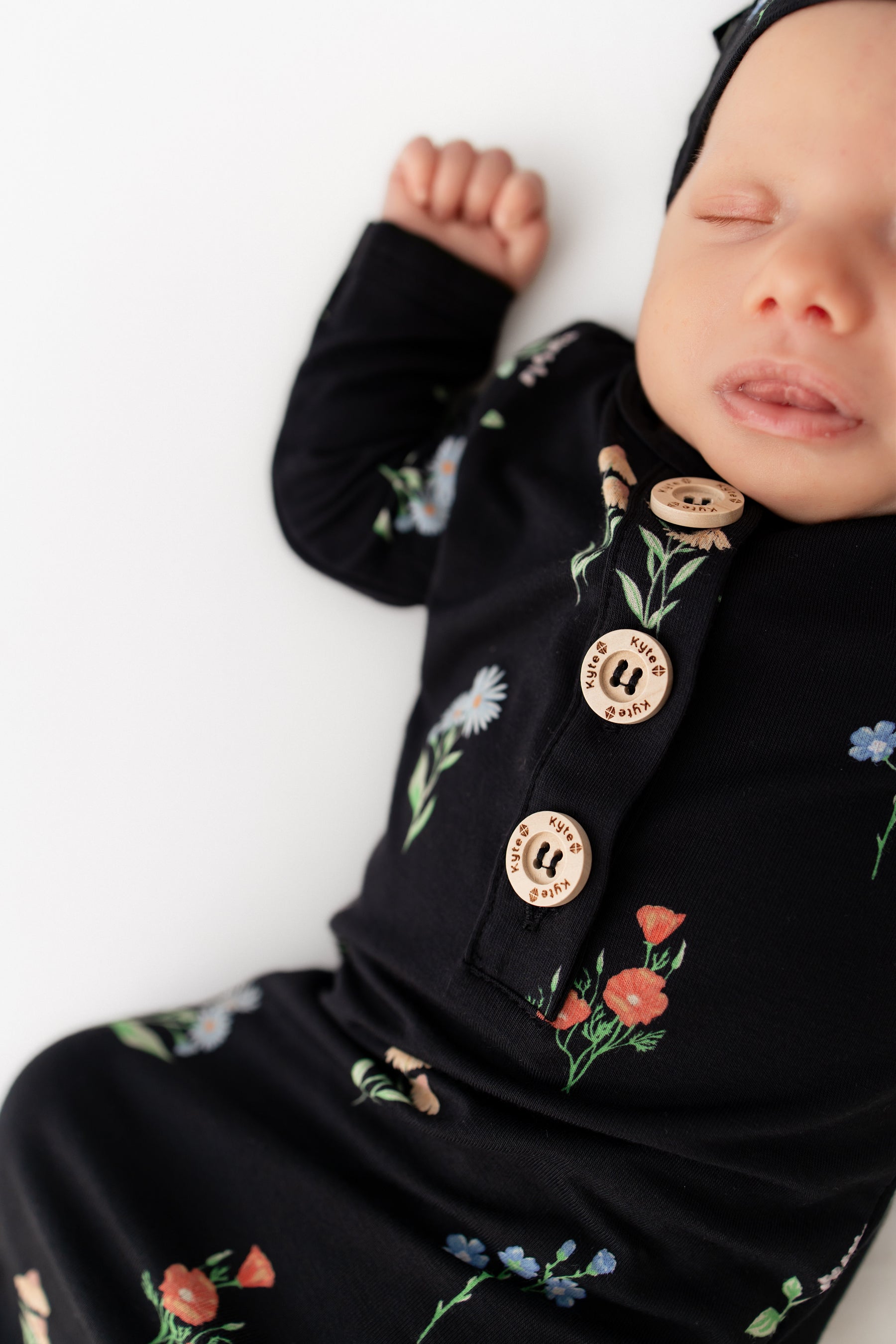 Baby sleeping in Knotted Gown with Hat Set in Midnight Wildflower print on a white background