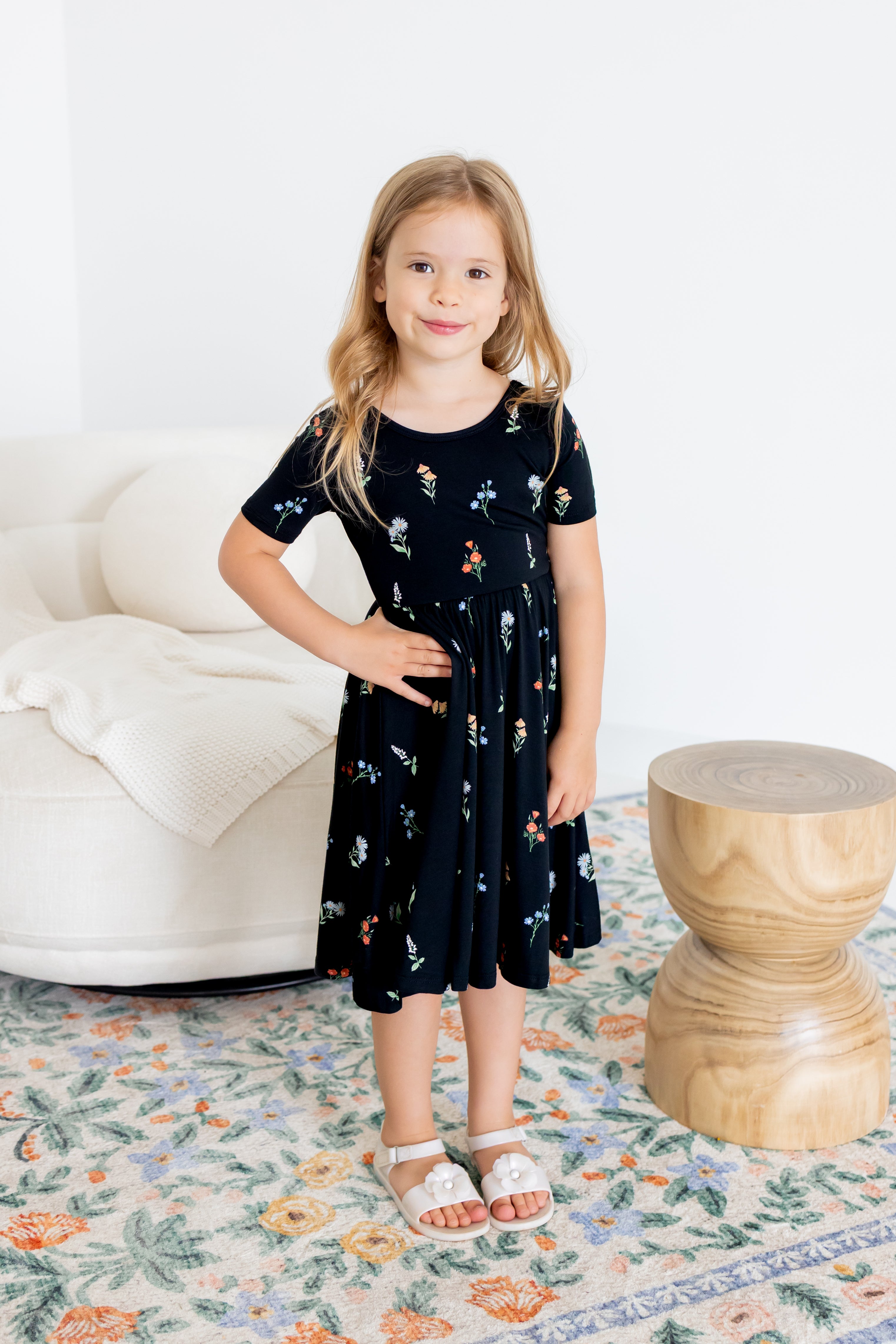 Girl wearing Twirl Dress in Midnight Wildflower print and white sandals standing in a living room