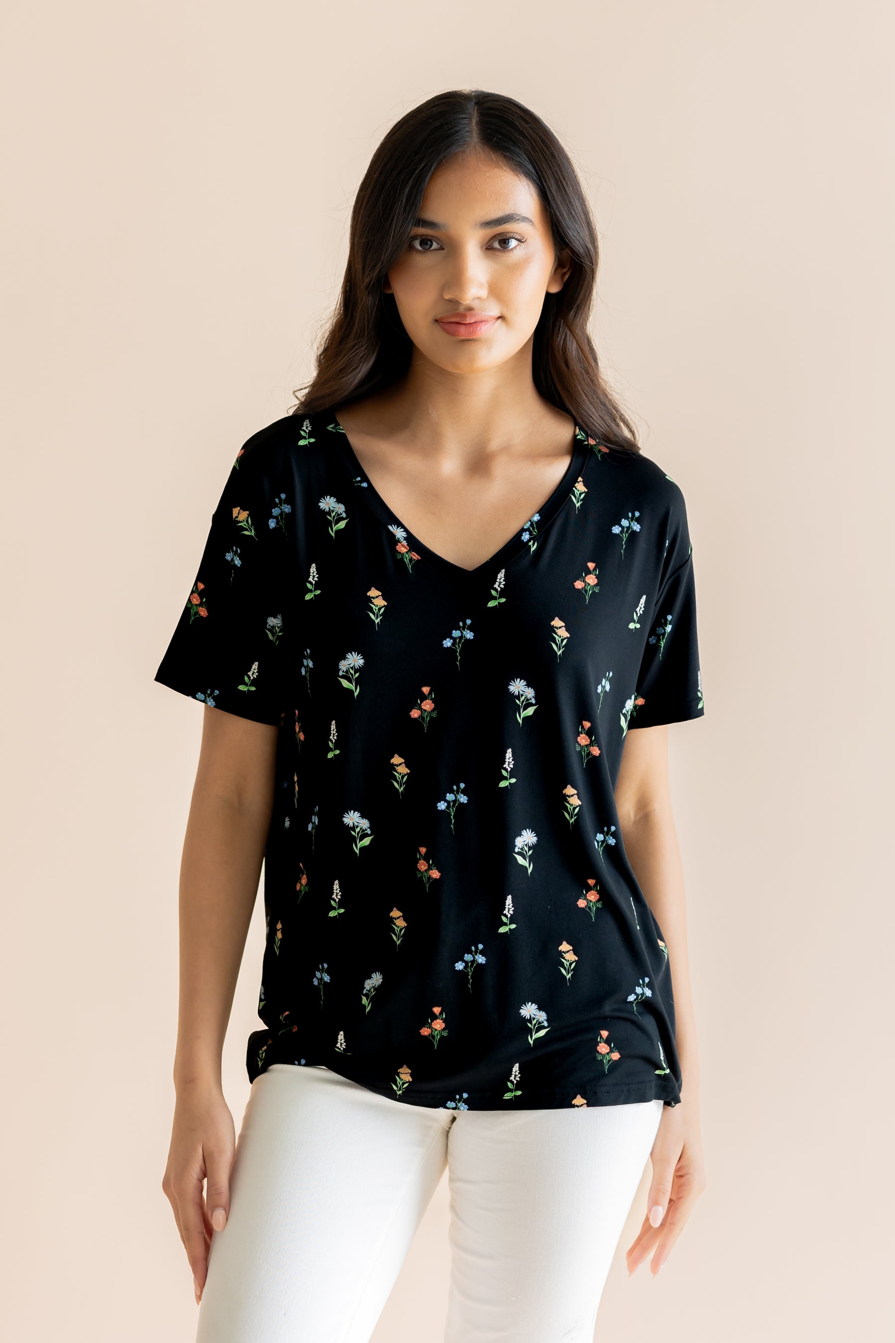 Model wearing Women's Relaxed Fit V-Neck in Midnight Wildflower print over white pants on a beige background