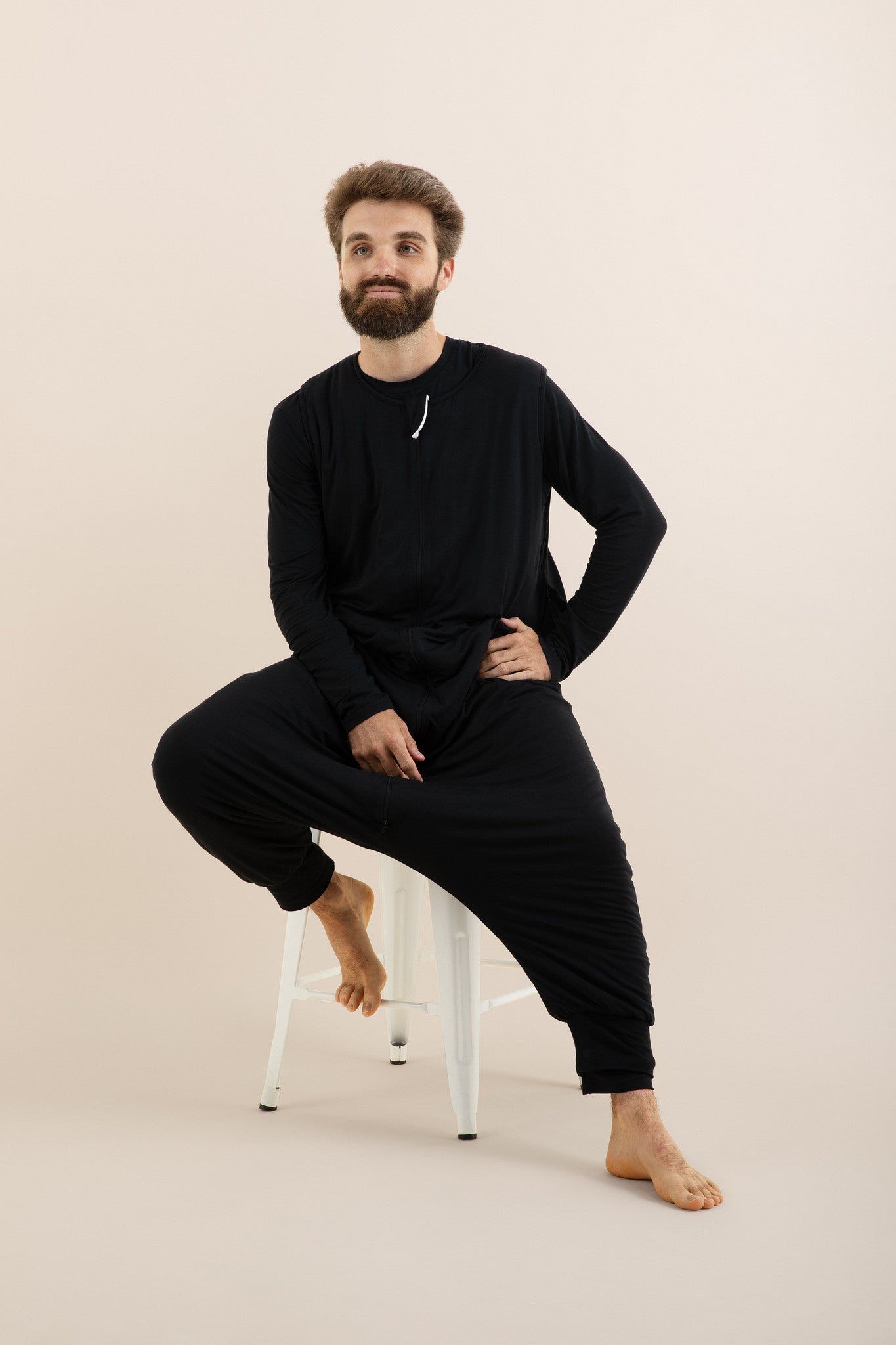Male model sitting on a white stool wearing the Adult Sleep Bag Walker in Midnight