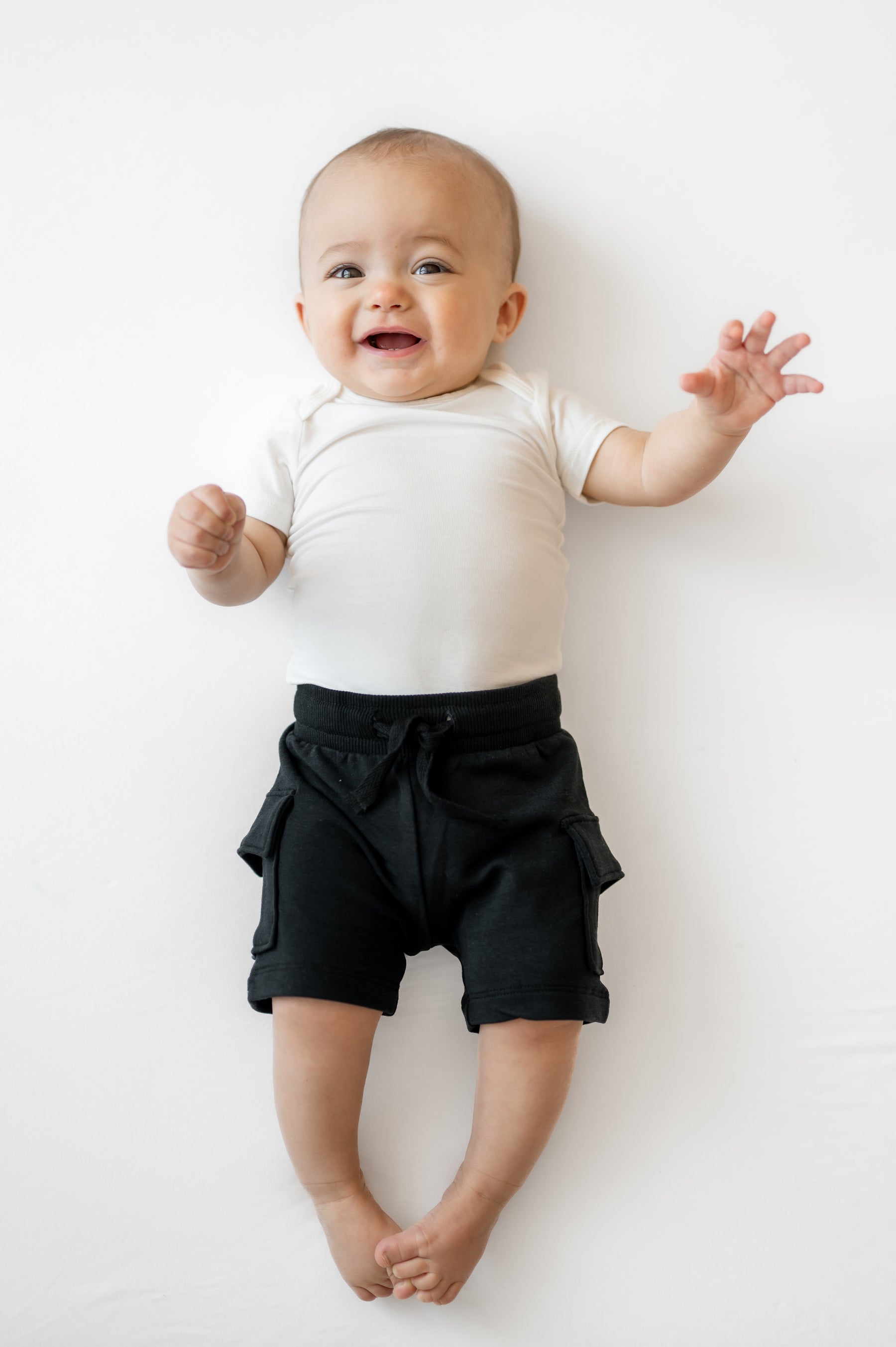 Infant laying on a white surface wearing the Cargo Short in Midnight with a white short sleeve bodysuit