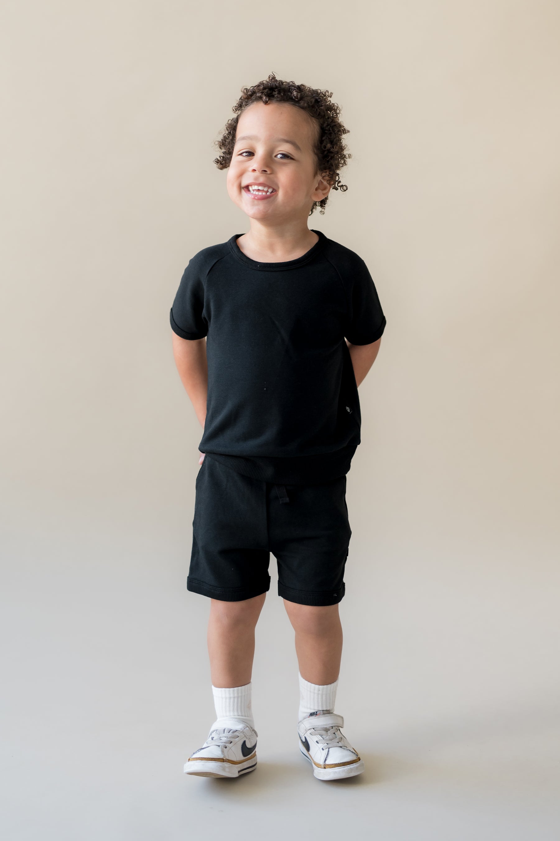 Young boy smiling with his hands behind his back wearing the Short Sleeve Jogger Set in Midnight
