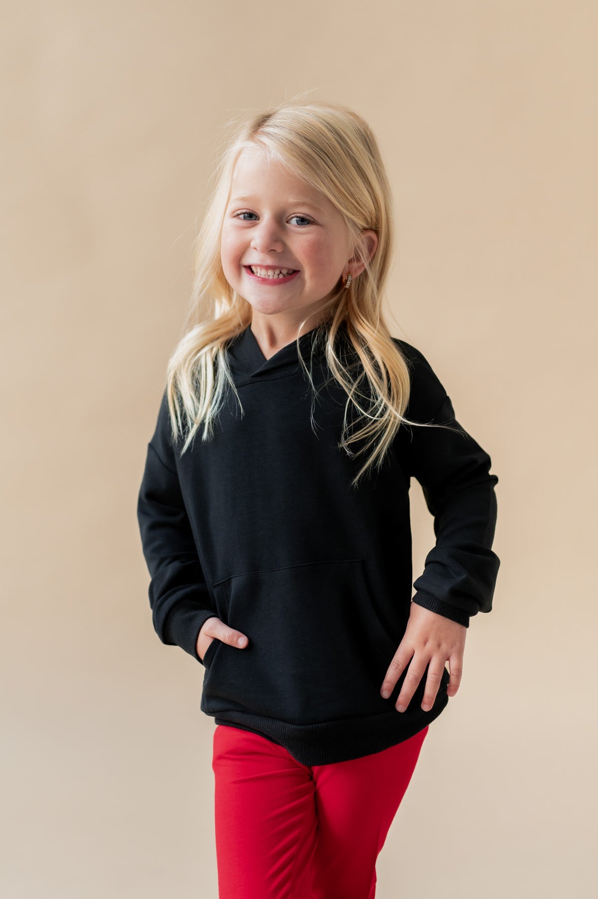 Girl smiling wearing Hoodie in Midnight color over red pants on a beige background