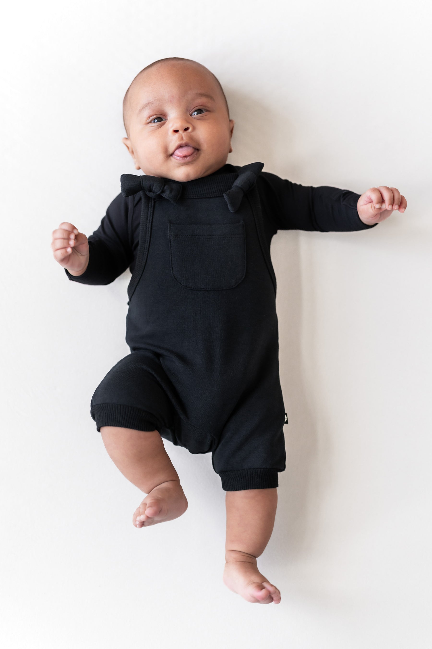 Baby wearing Overall in Midnight color lying on a beige background