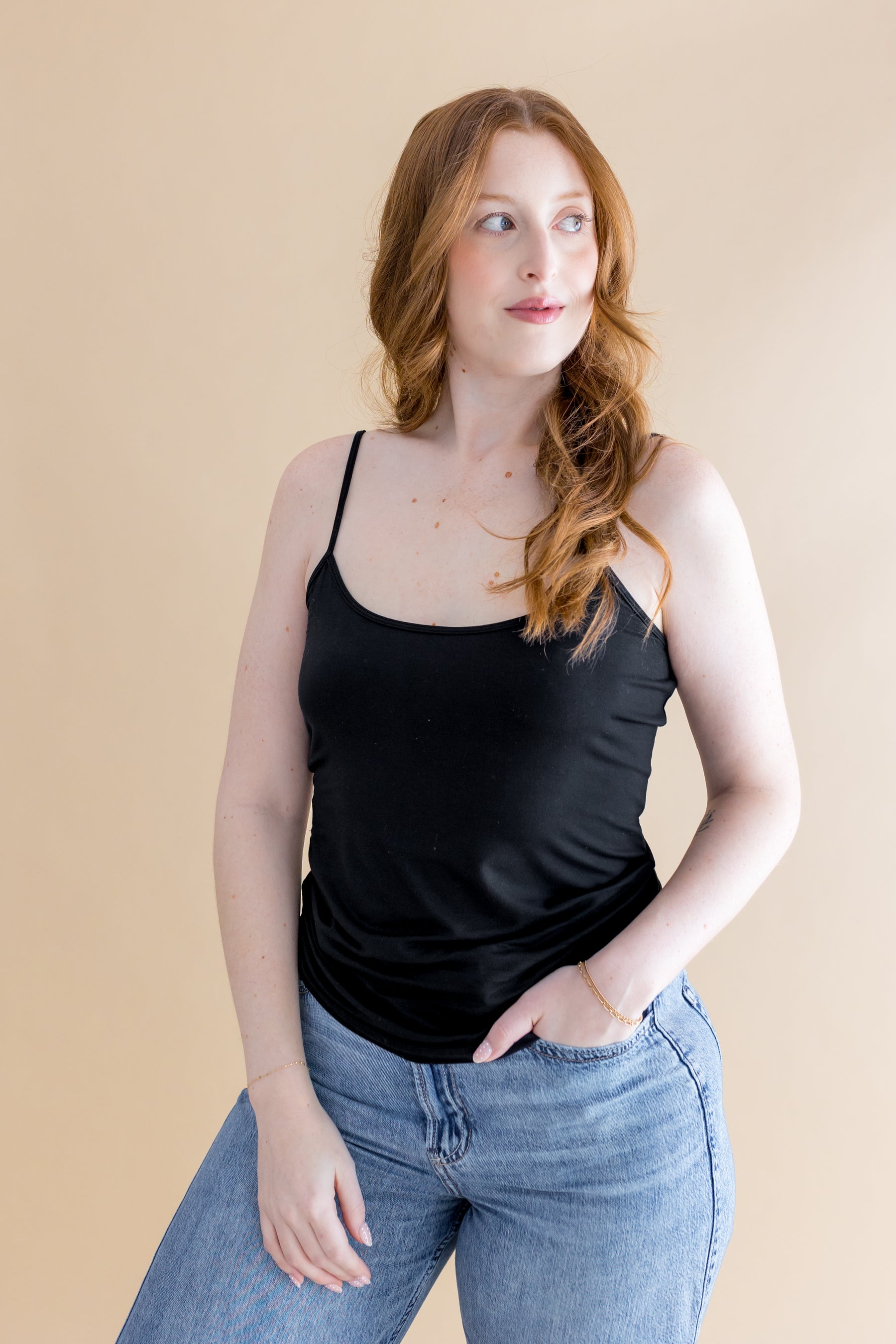 Woman wearing a black tank top and blue jeans against a beige background