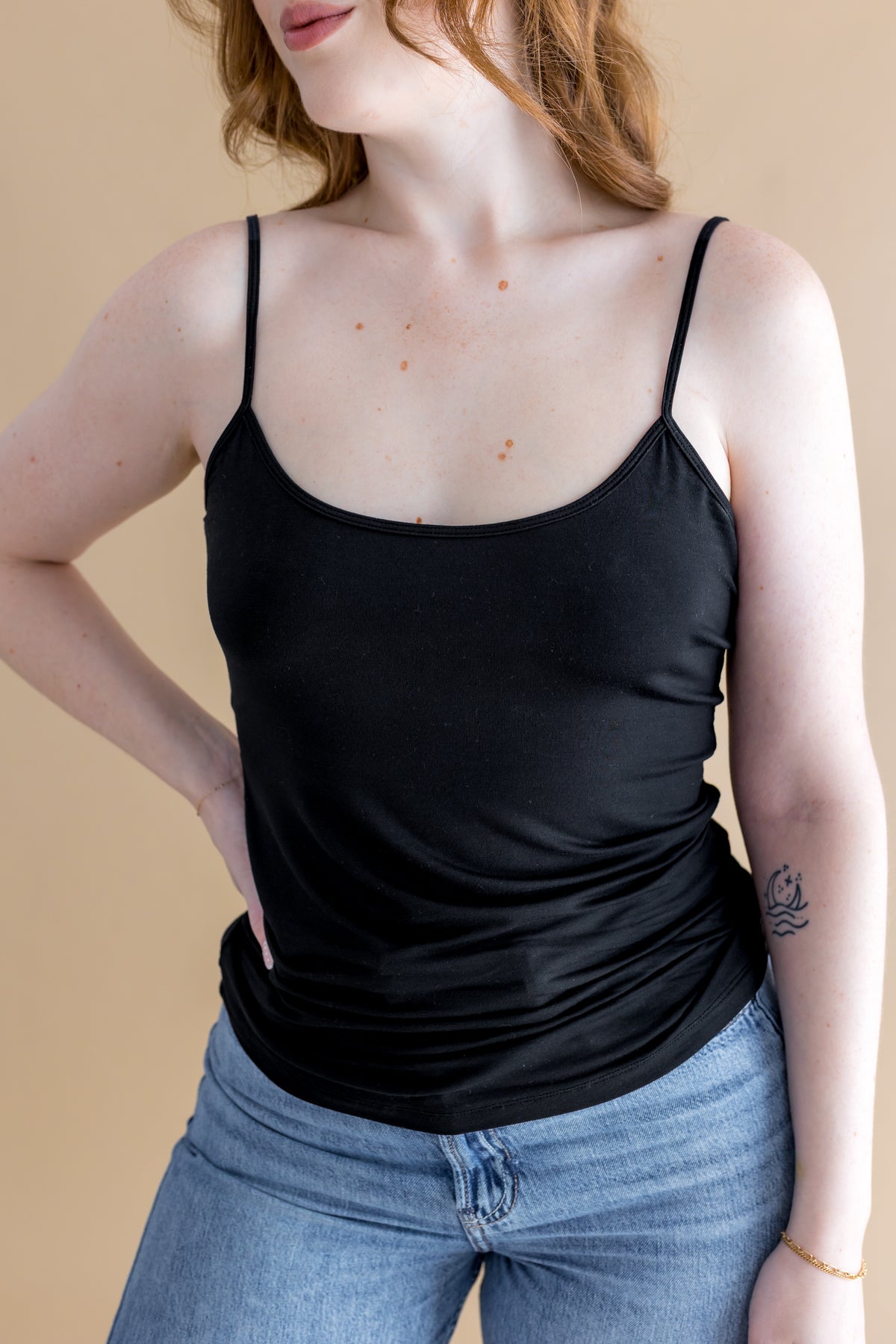 Person wearing a black tank top and blue jeans against a beige background