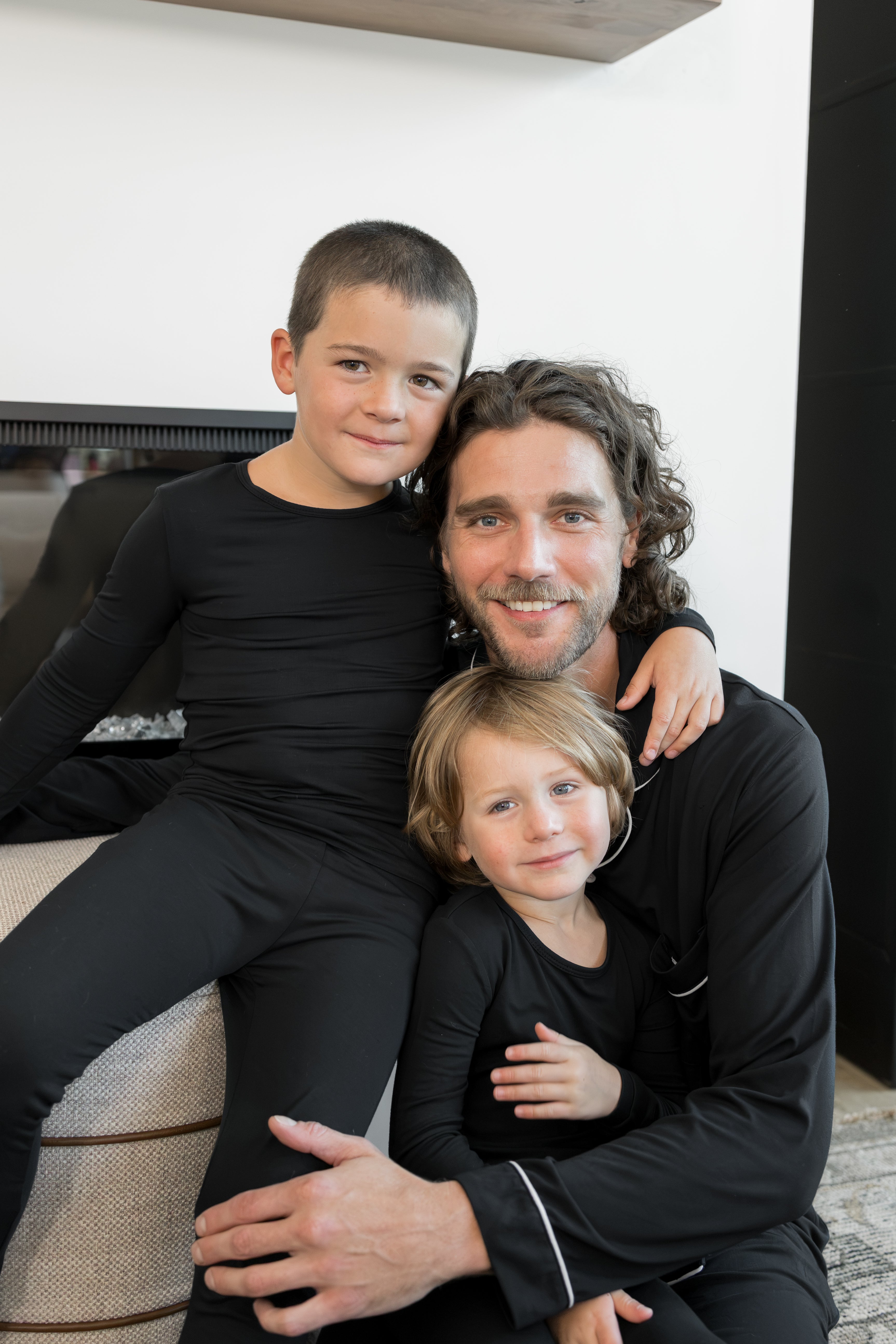 A man and two children wearing matching black long-sleeve activewear sets pose together in a modern indoor setting.