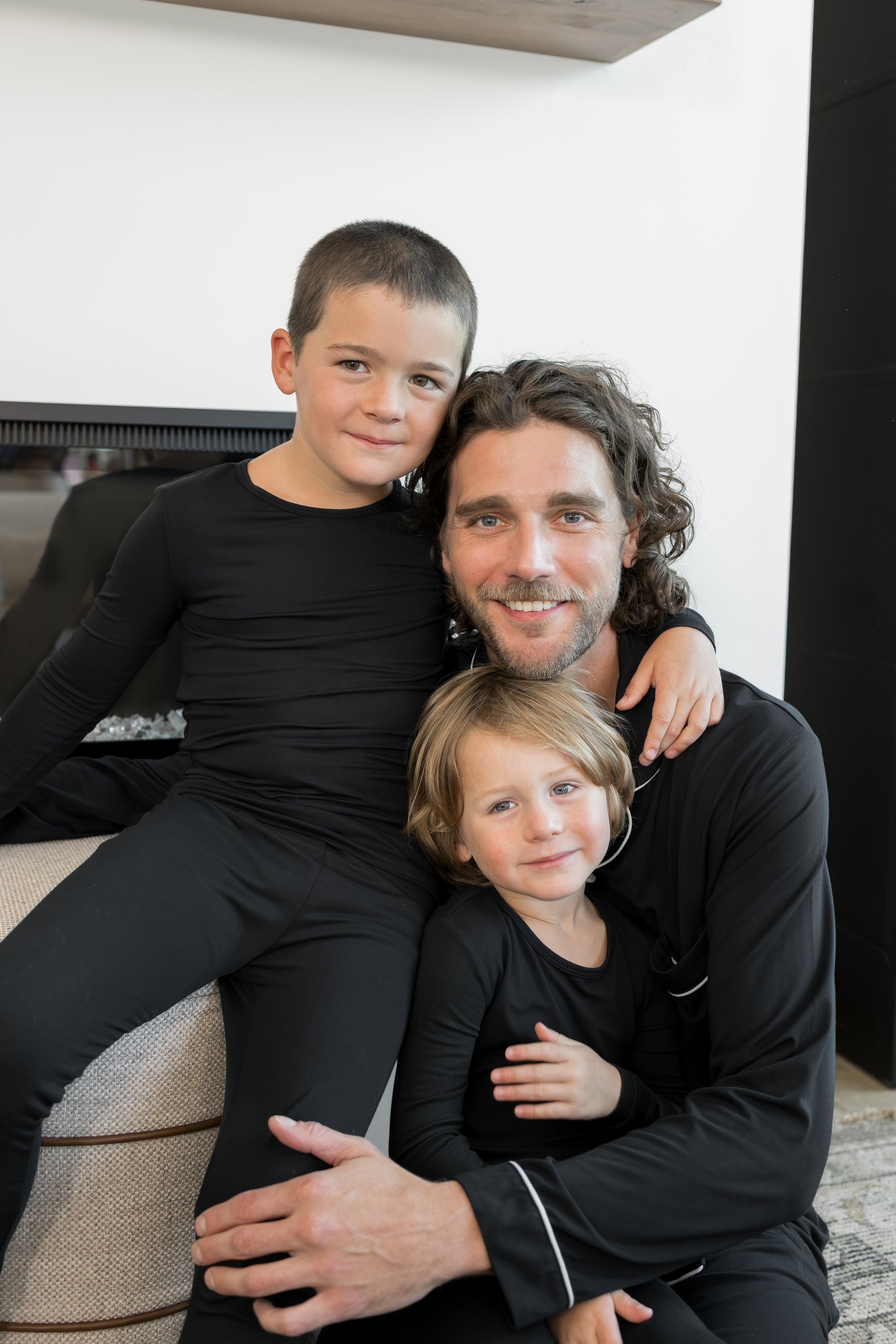 A man and two children wearing matching black long-sleeve activewear sets pose together in a modern indoor setting.
