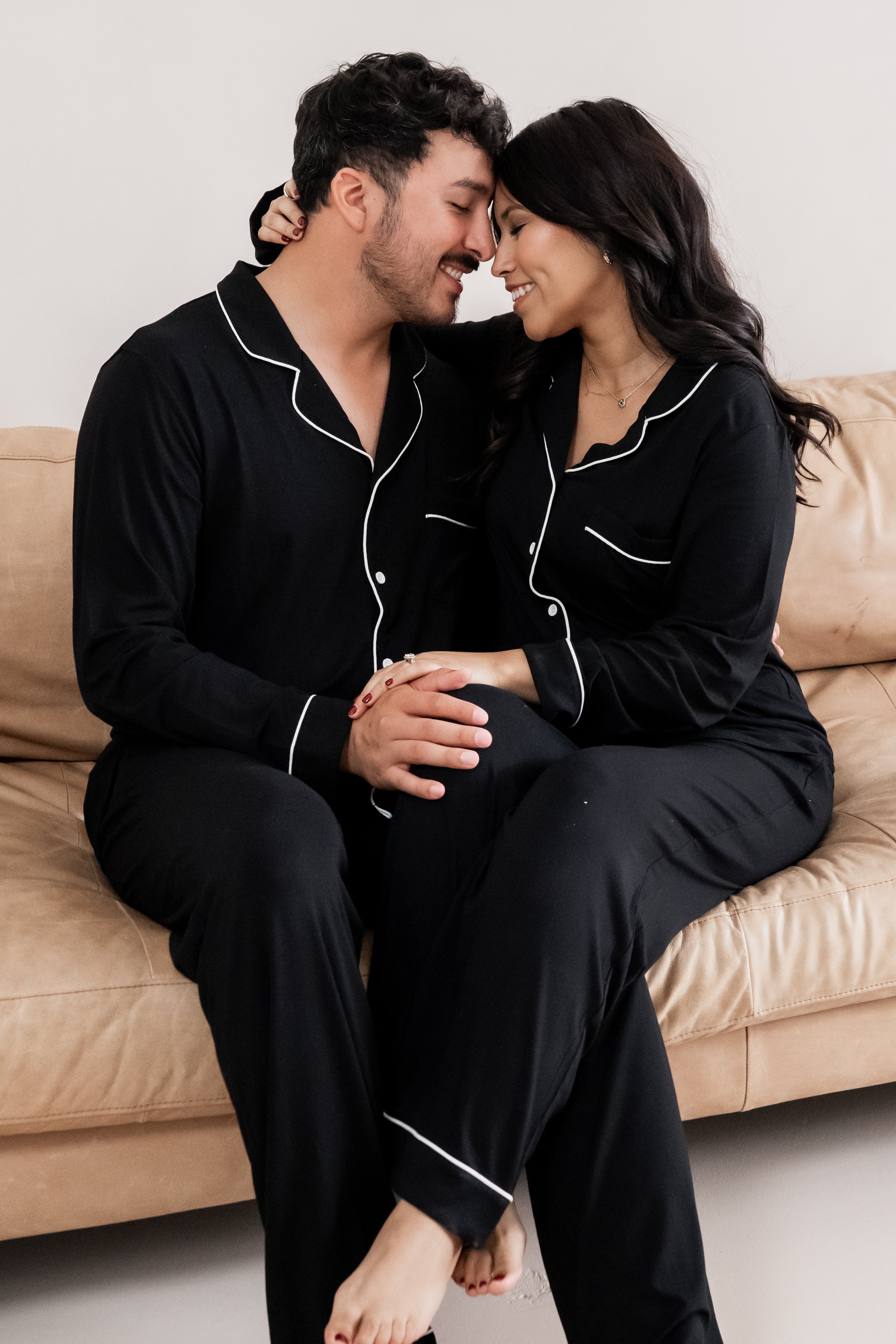 Husband and wife sitting on a couch with their foreheads touching both matching in Long Sleeve Midnight Pajamas with Cloud Trim