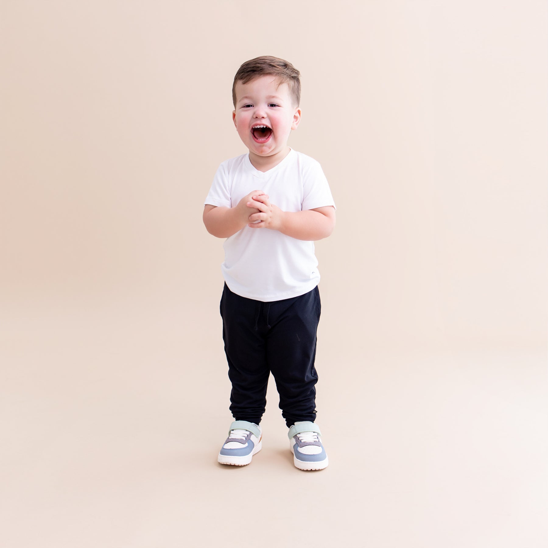 Smiling toddler standing in front of a light beige background wearing the Toddler Jogger Pant in Midnight with a white v-neck shirt